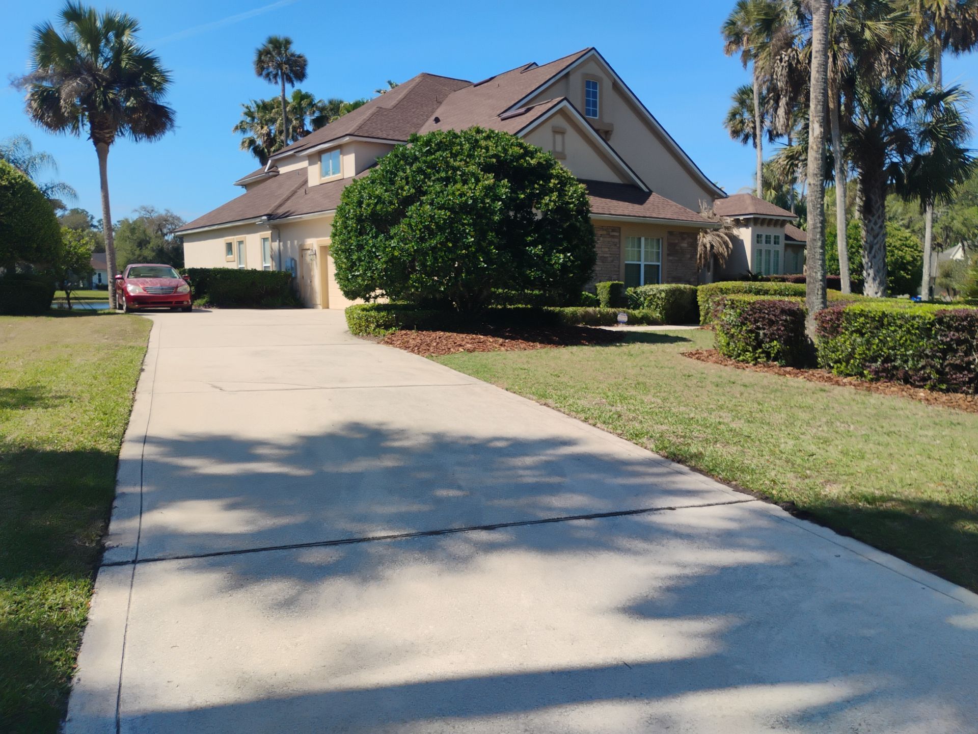 Suburban house with a long driveway, palm trees, and a red car parked on the left