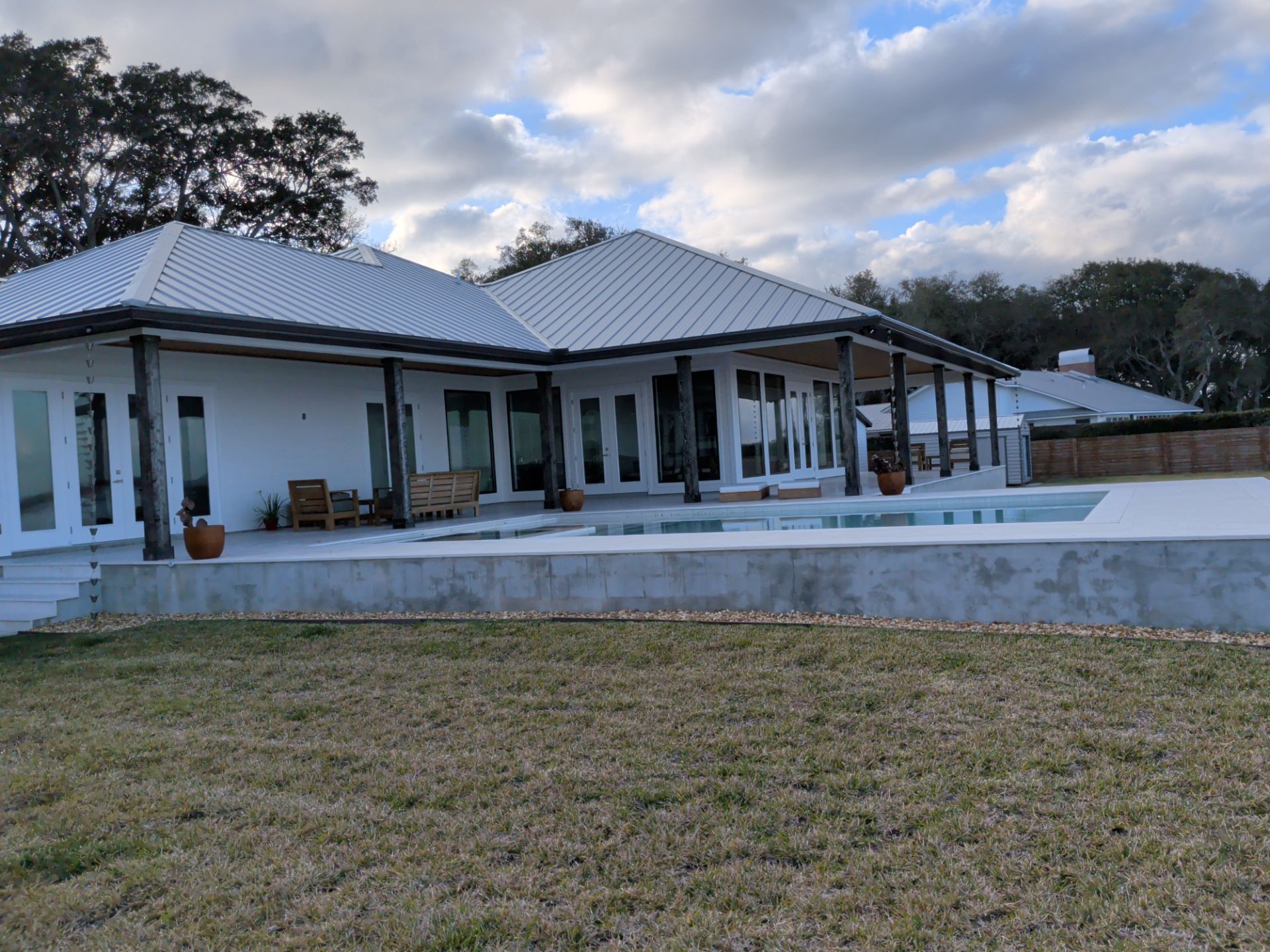Modern single-story house with a gray metal roof, white porch columns, and a front lawn.