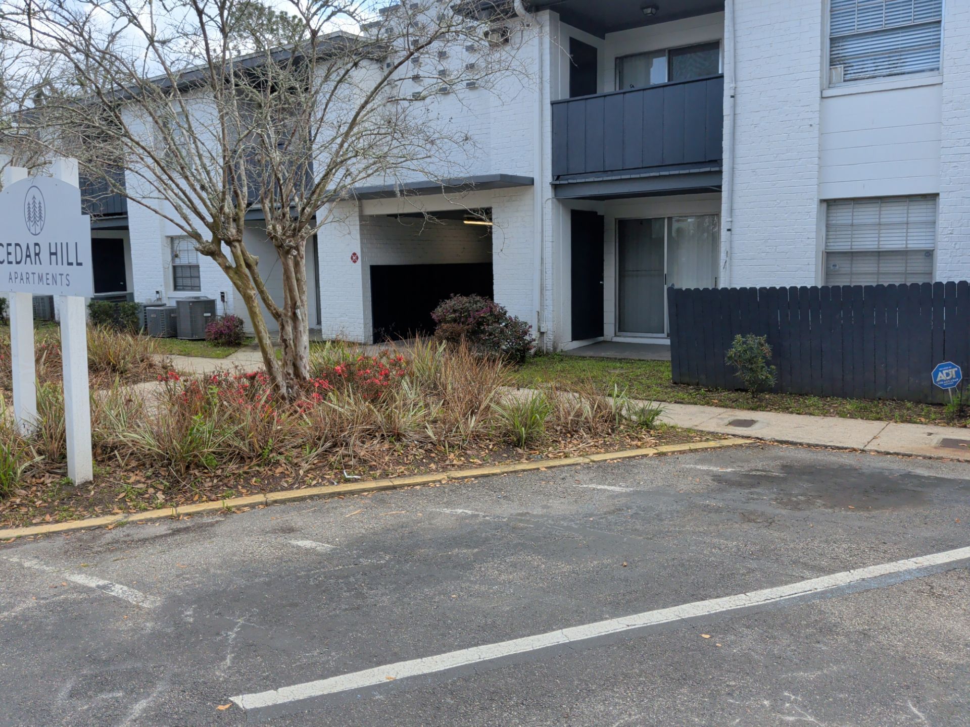 Apartment building entrance with parking spaces, shrubs, and a sign in front