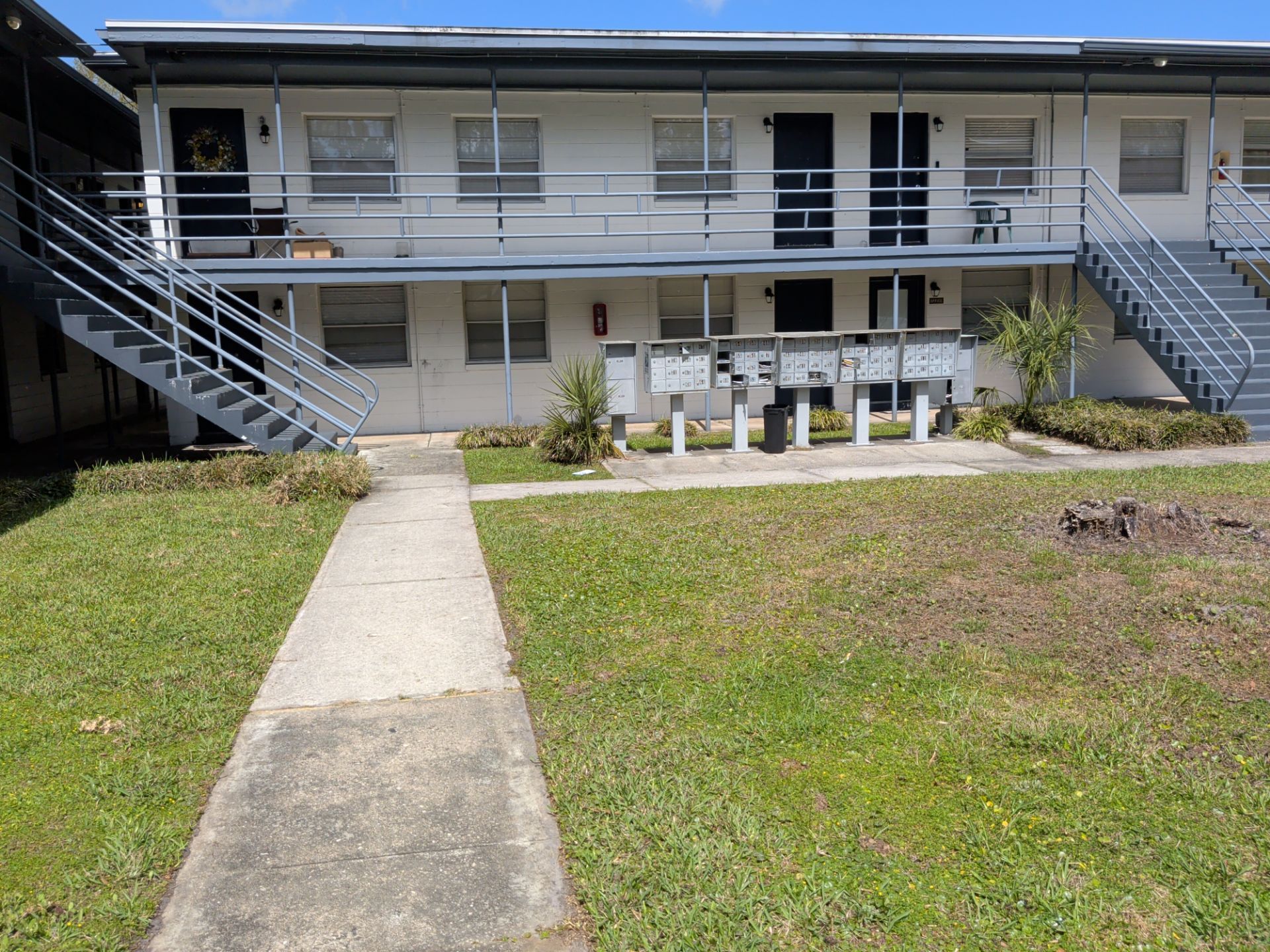 Apartment building exterior with central walkway, staircases on both ends, and a grassy courtyard