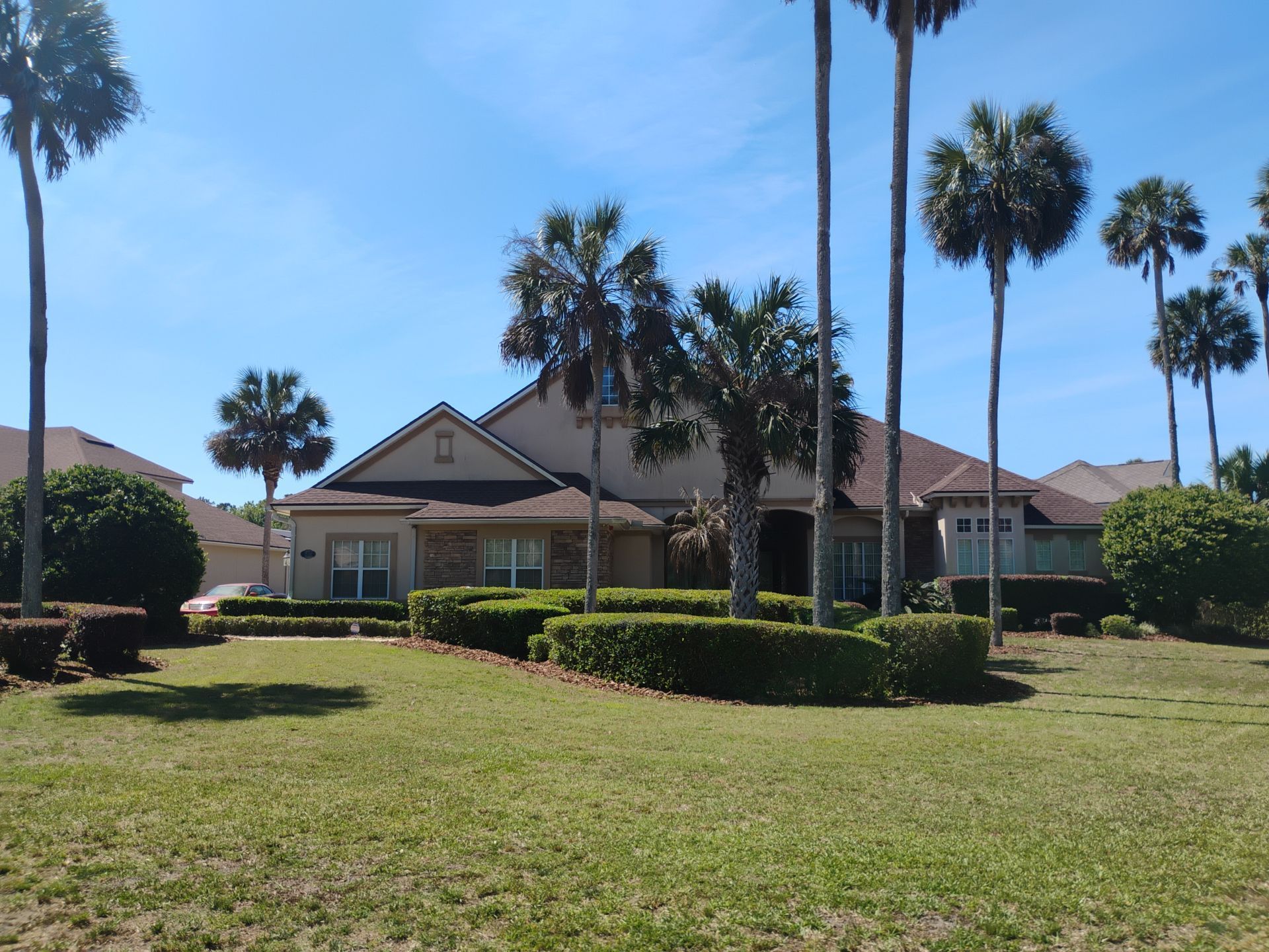 Single-story house with red roof, palm trees, and a green lawn under a clear blue sky.