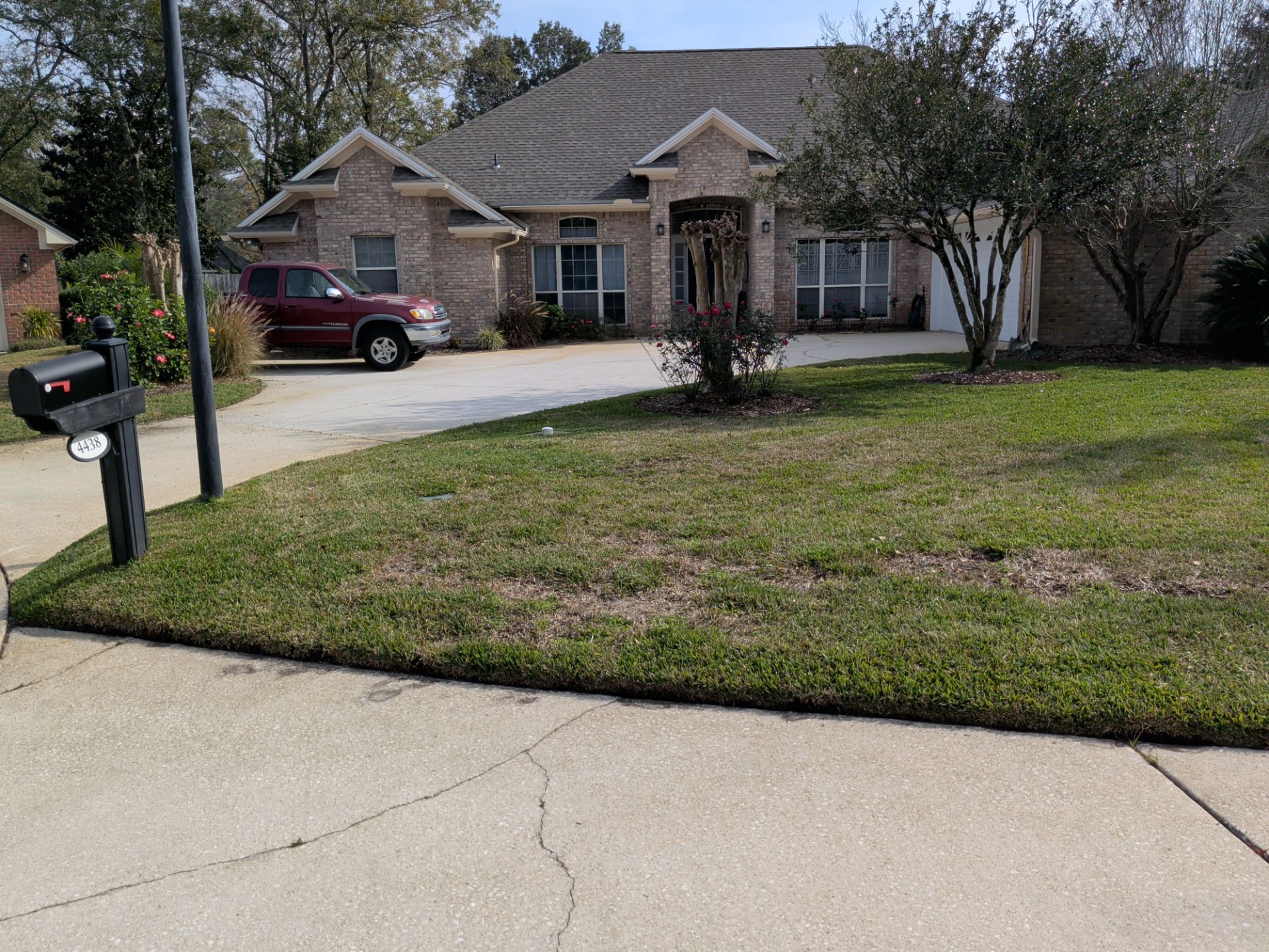 Suburban brick house with driveway, parked red SUV, mailbox, and front lawn