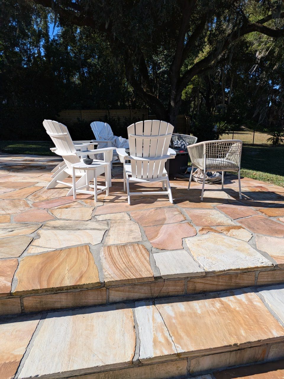 White patio chairs around a table on a stone terrace in a sunny backyard garden