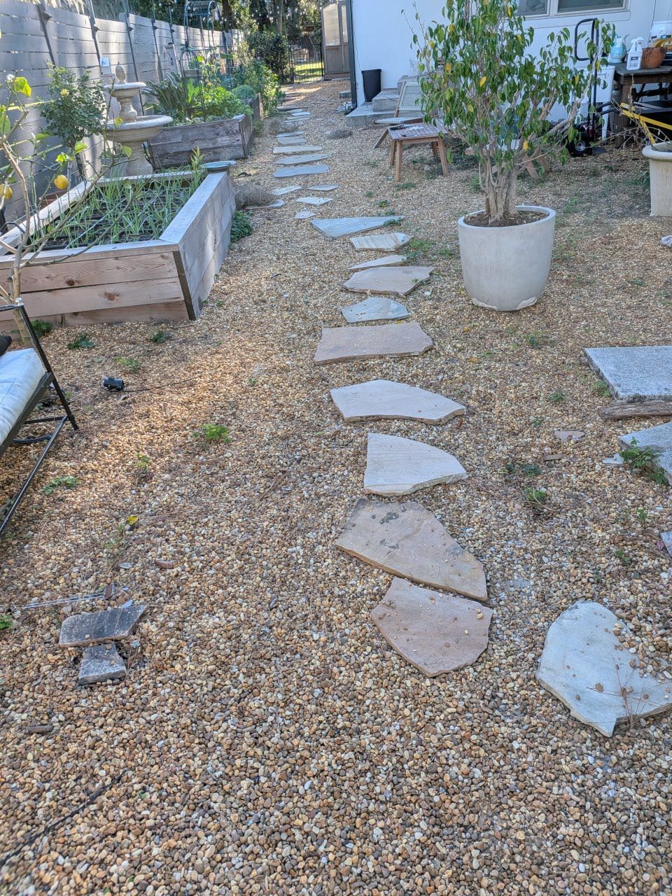 Gravel garden path with stepping stones between raised beds and potted plants.