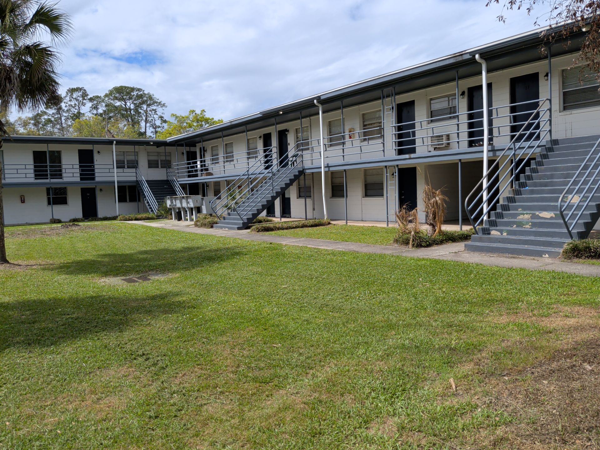 Two-story apartment building with exterior staircases and a grassy courtyard