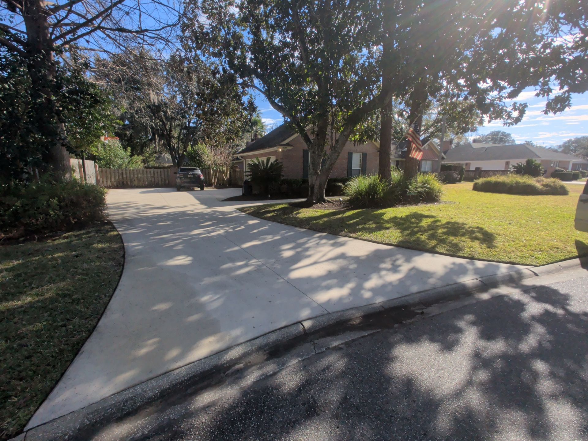 A house with a long, curved driveway under a sunny sky, surrounded by trees and lawn.