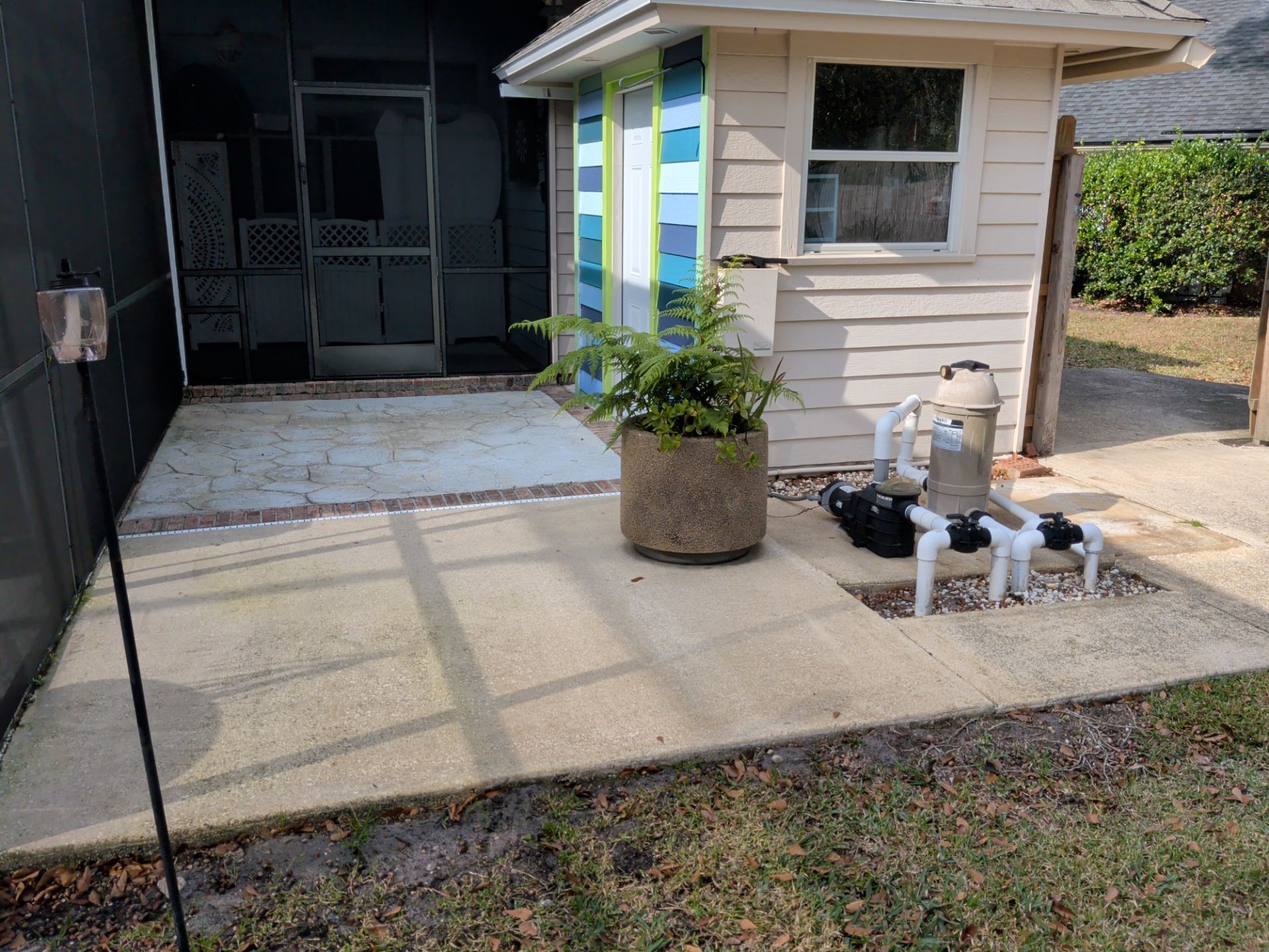 Small porch beside a house with potted plant, striped post, and utility pipes on a concrete patio.