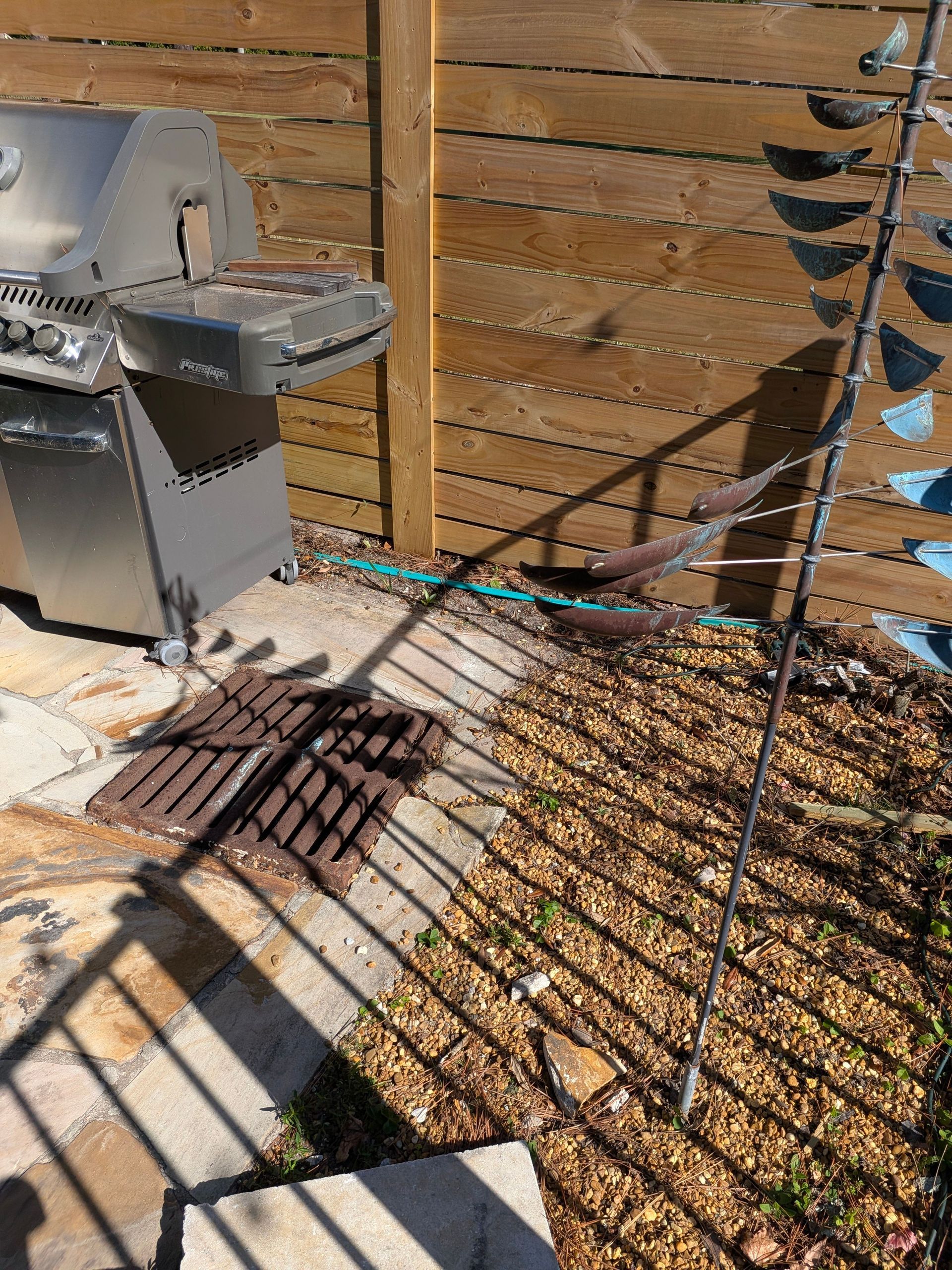 Outdoor grill beside a wooden fence, with sunlight casting a shadow across the patio.