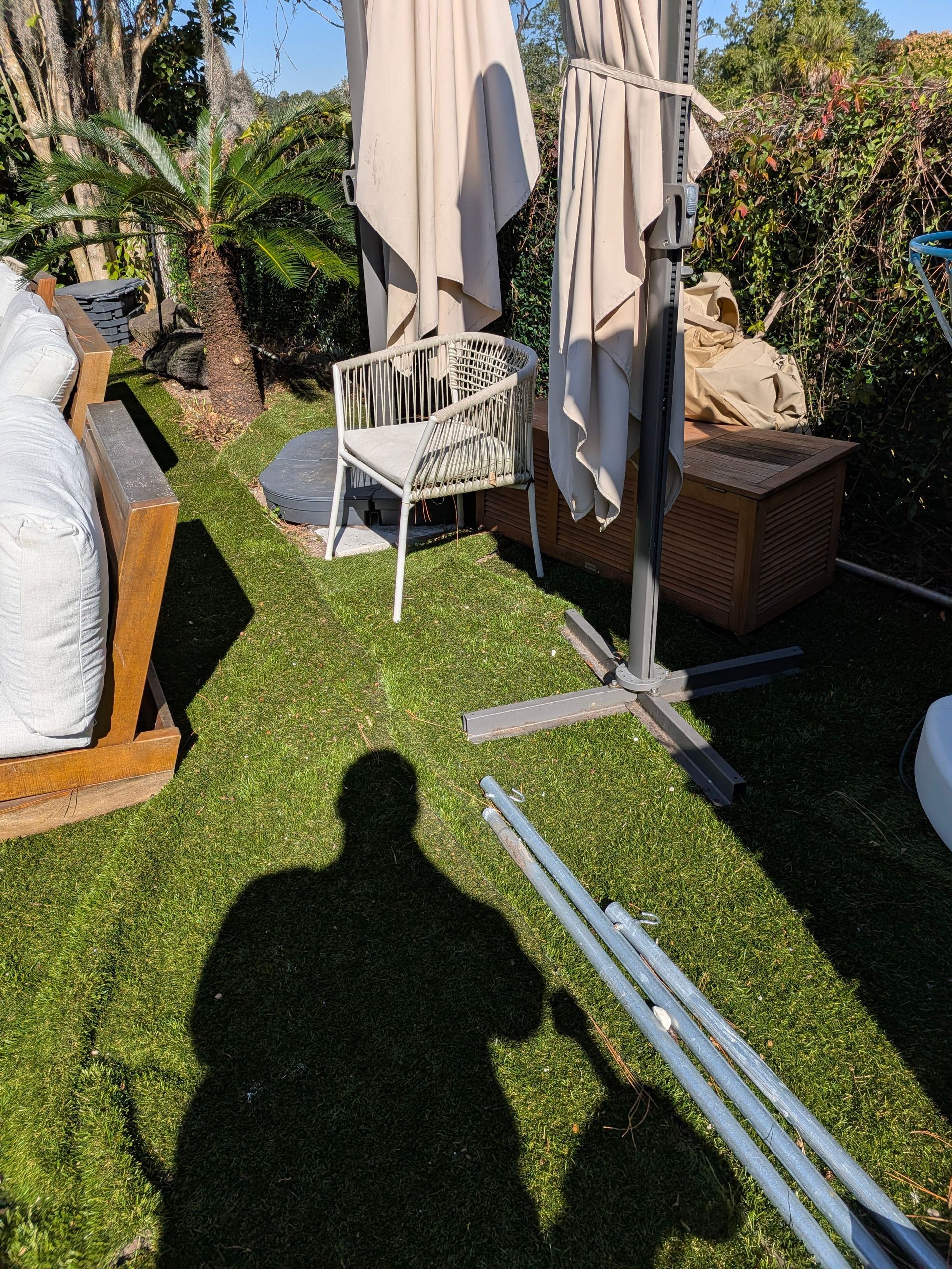 Outdoor patio with beige umbrella, white chair, wicker table, and garden plants on artificial grass.