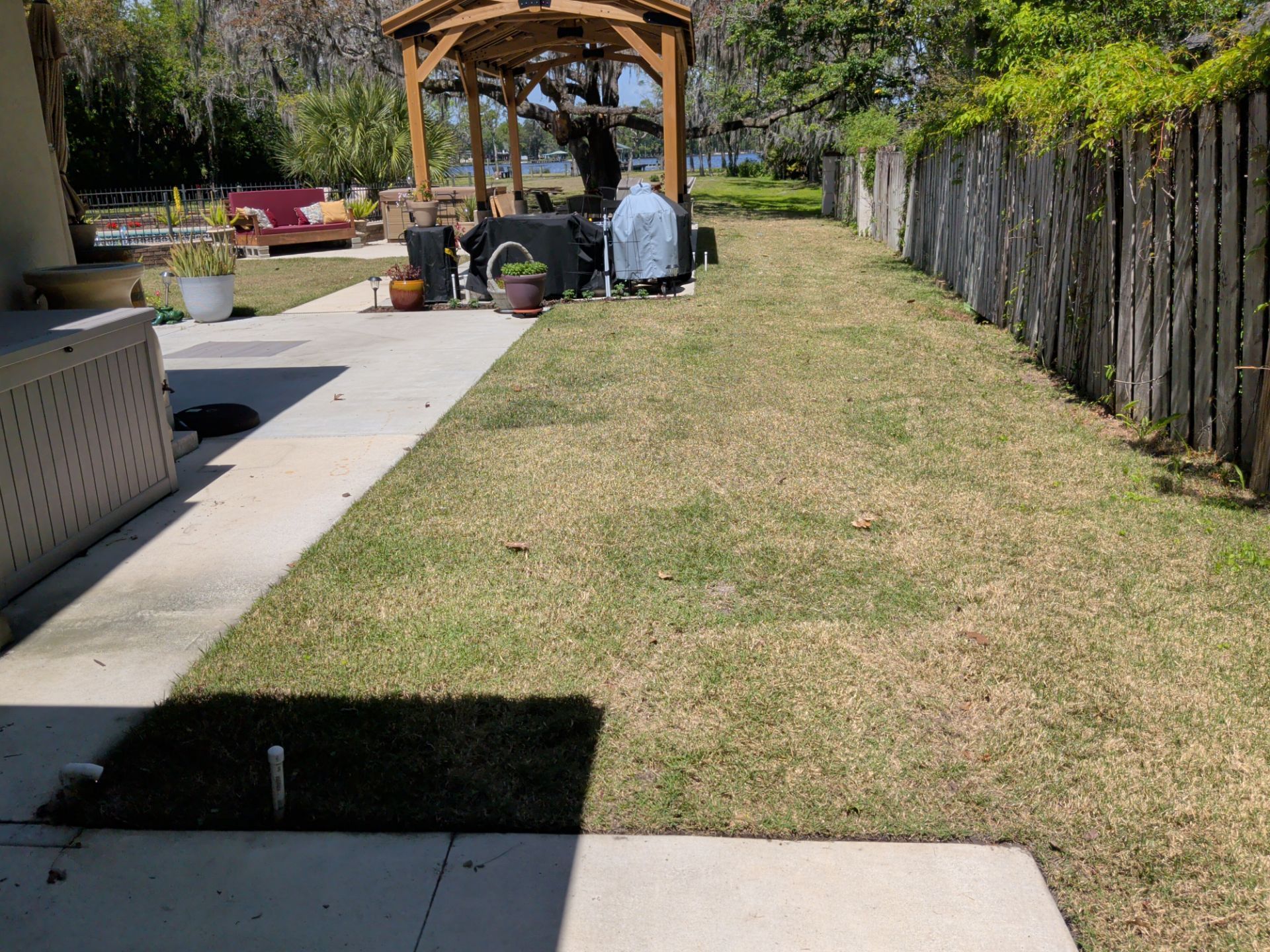 Backyard lawn with a wooden gazebo, patio, and people gathered in the distance