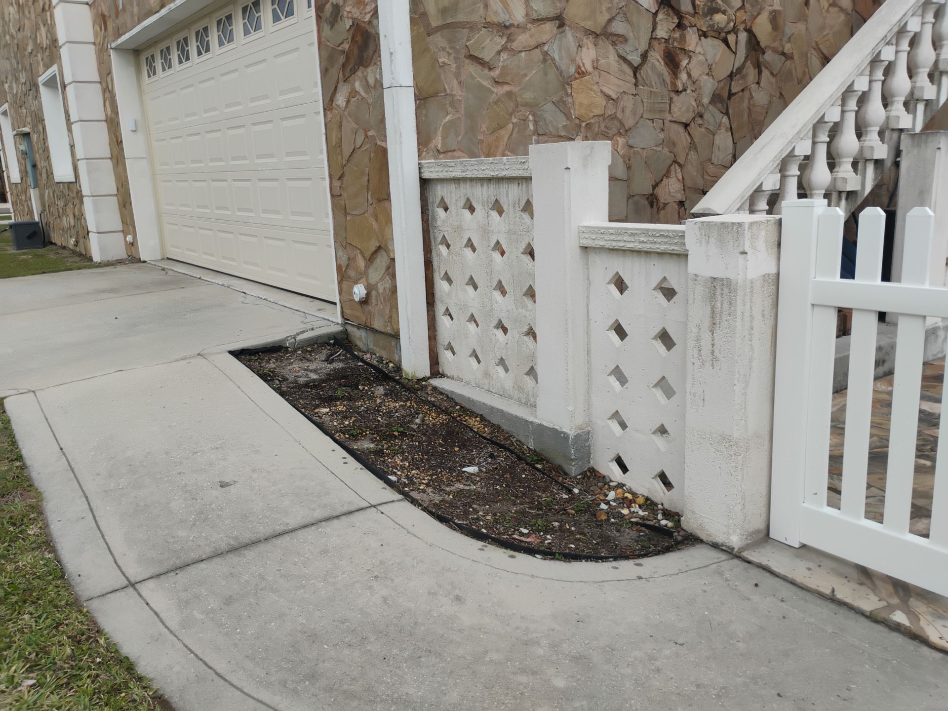Curved concrete driveway beside a stone house, garage door, and white fence