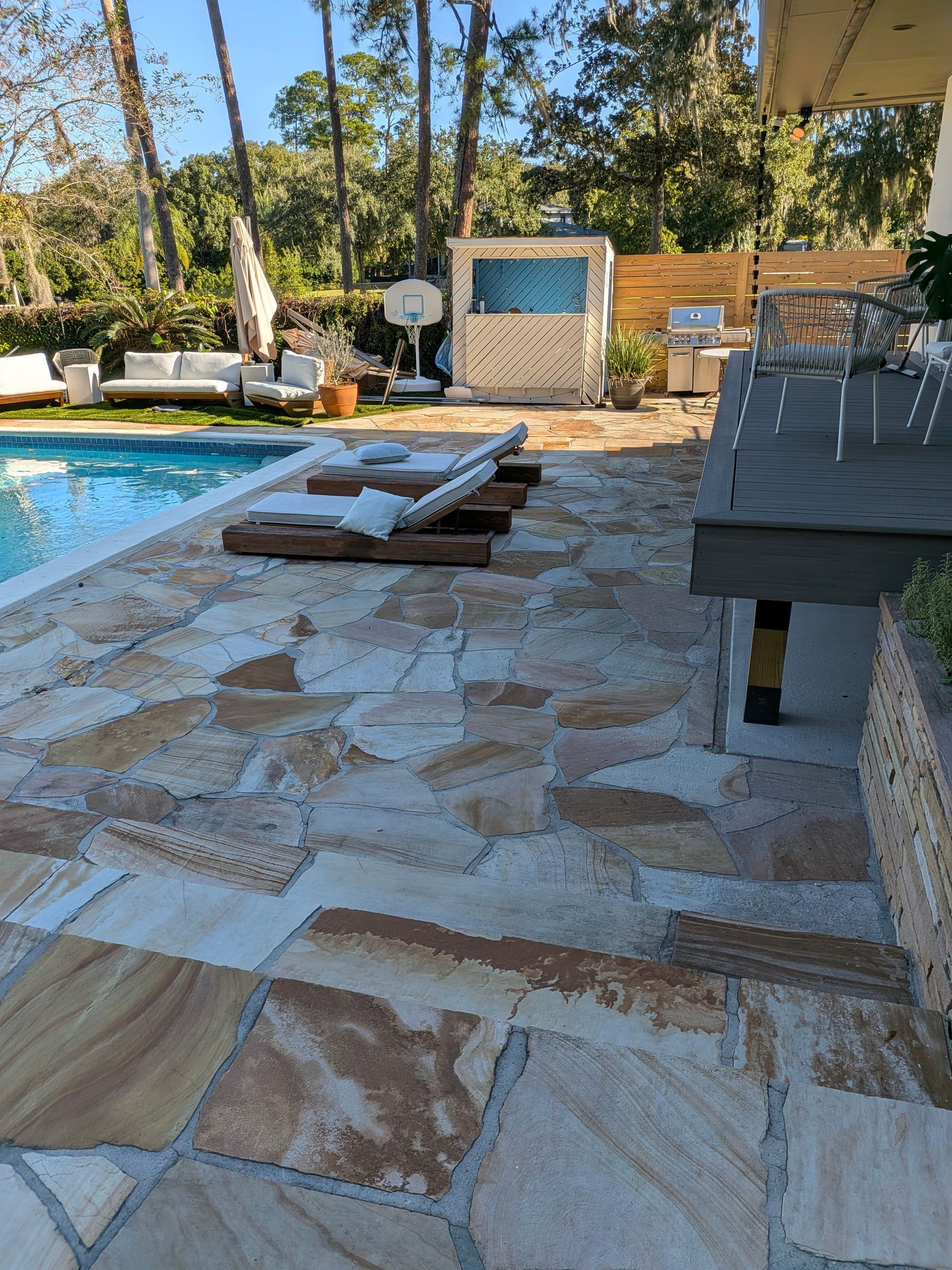 Backyard pool patio with stone paving, lounge chairs, and a small cabana in the shade