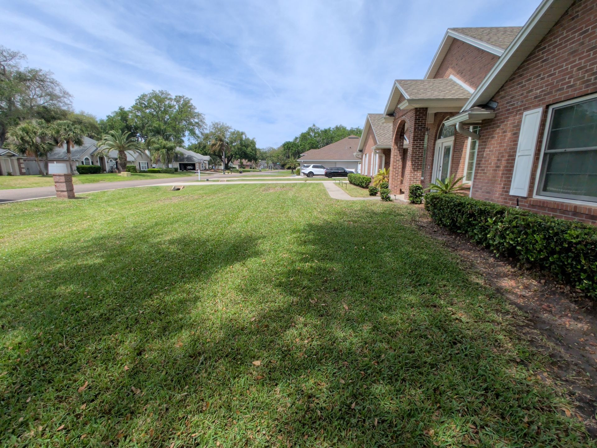 Suburban front yard with green lawn beside a brick house under a partly cloudy sky