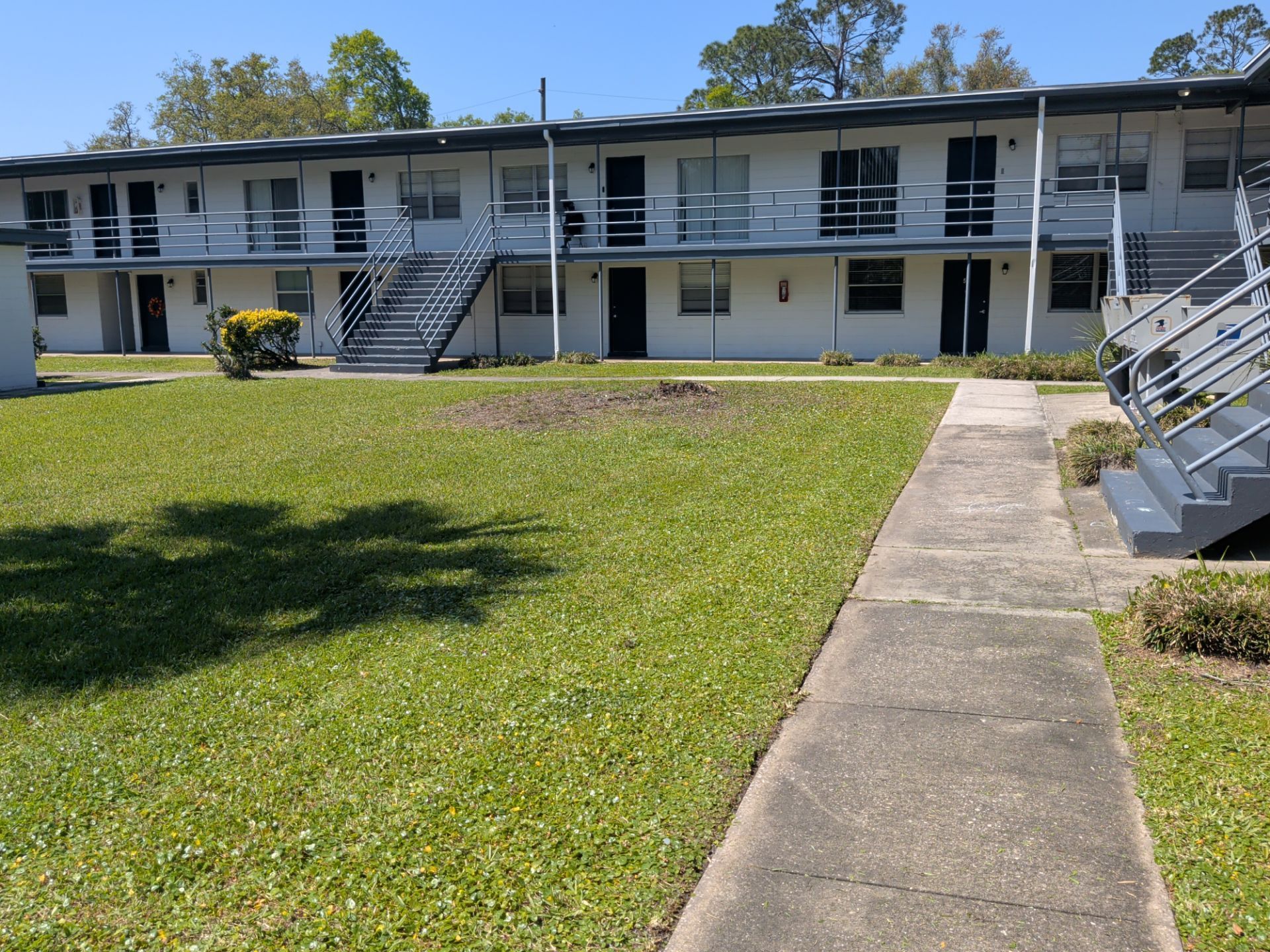 Motel-style apartment building with exterior stairs and a grassy courtyard with a concrete walkway
