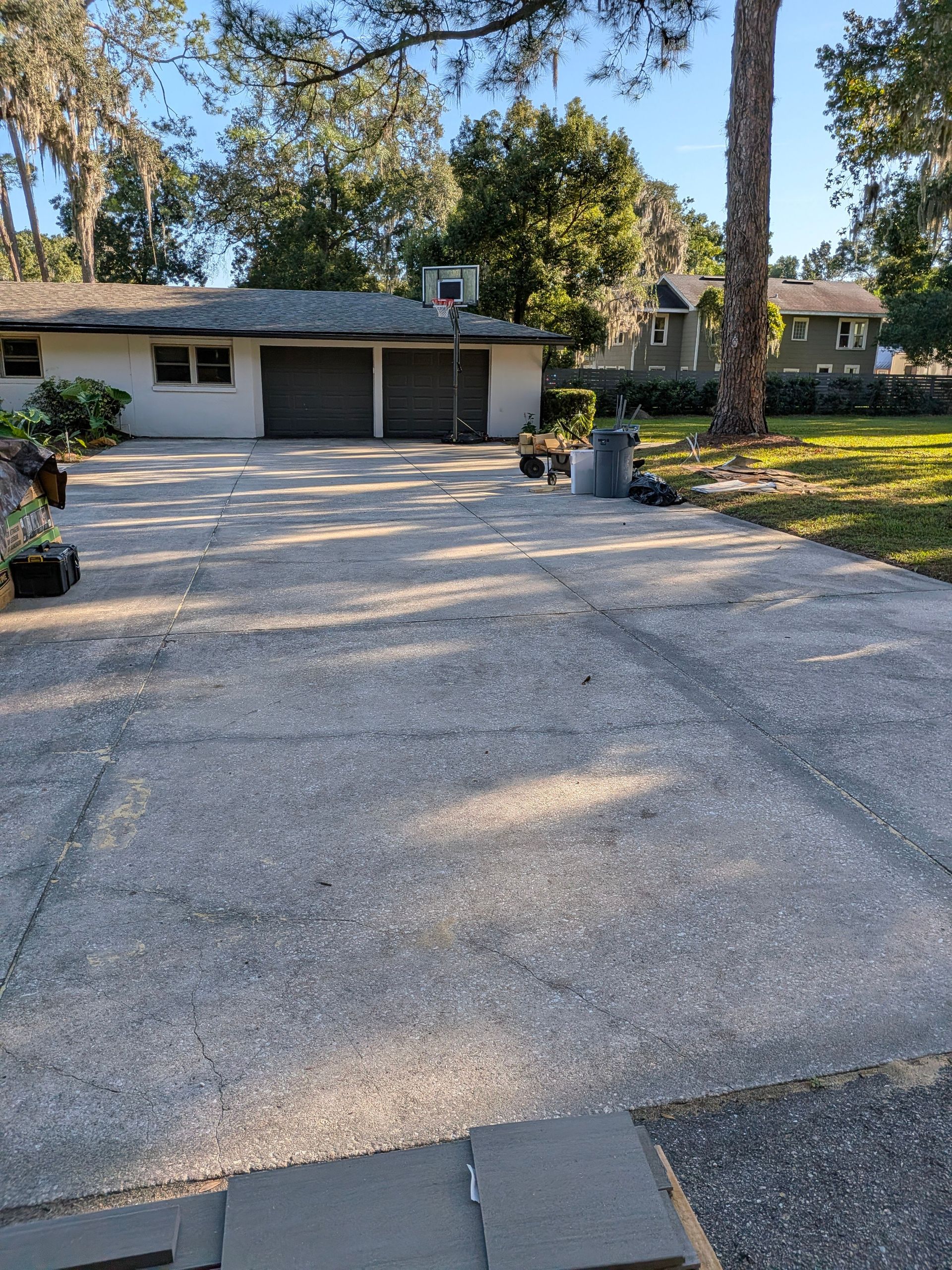 Gravel driveway leading to a single-story house with a basketball hoop and trees in the yard