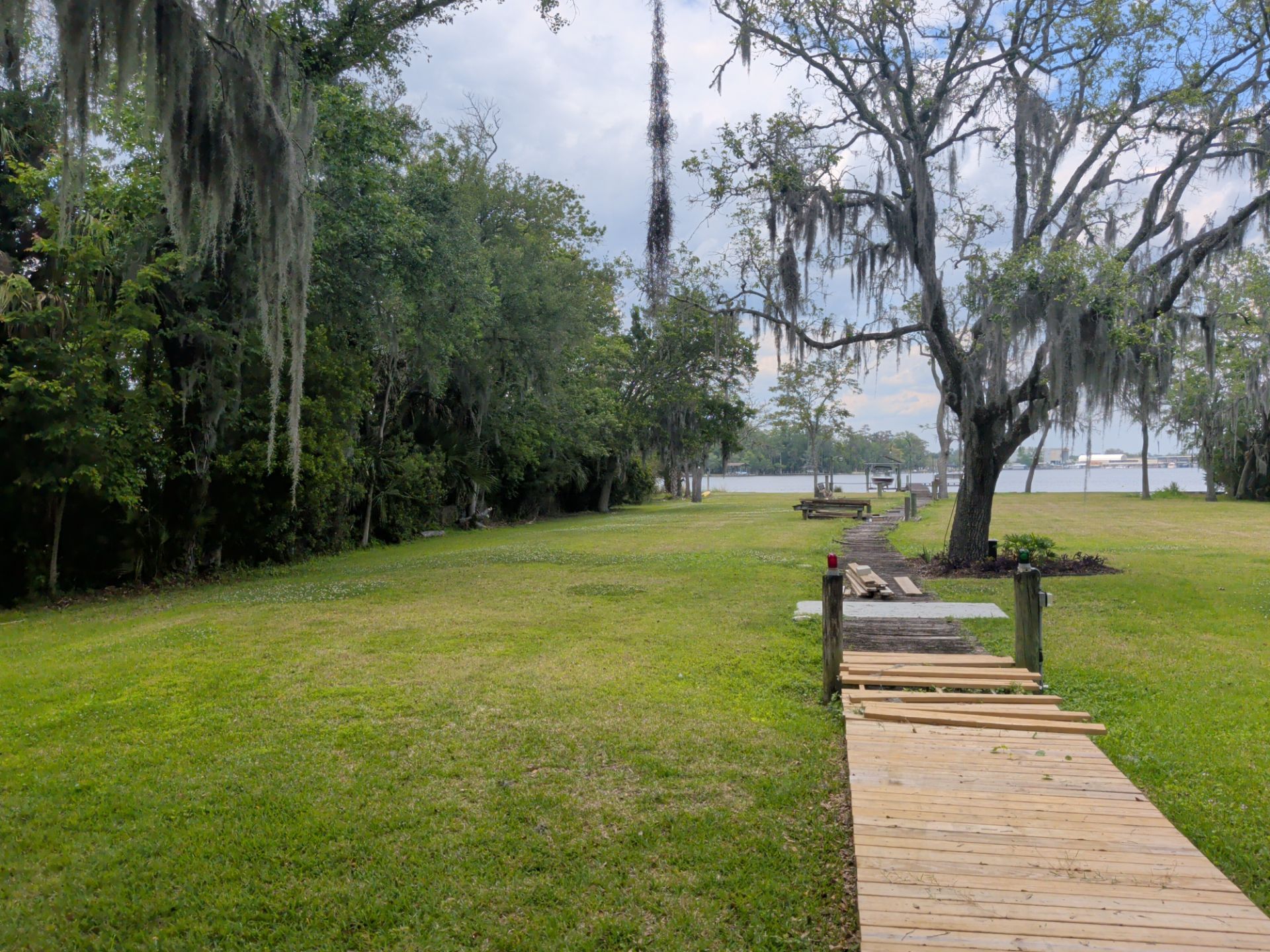 Grassy waterfront yard with a wooden dock path, trees, and a single large tree near the water