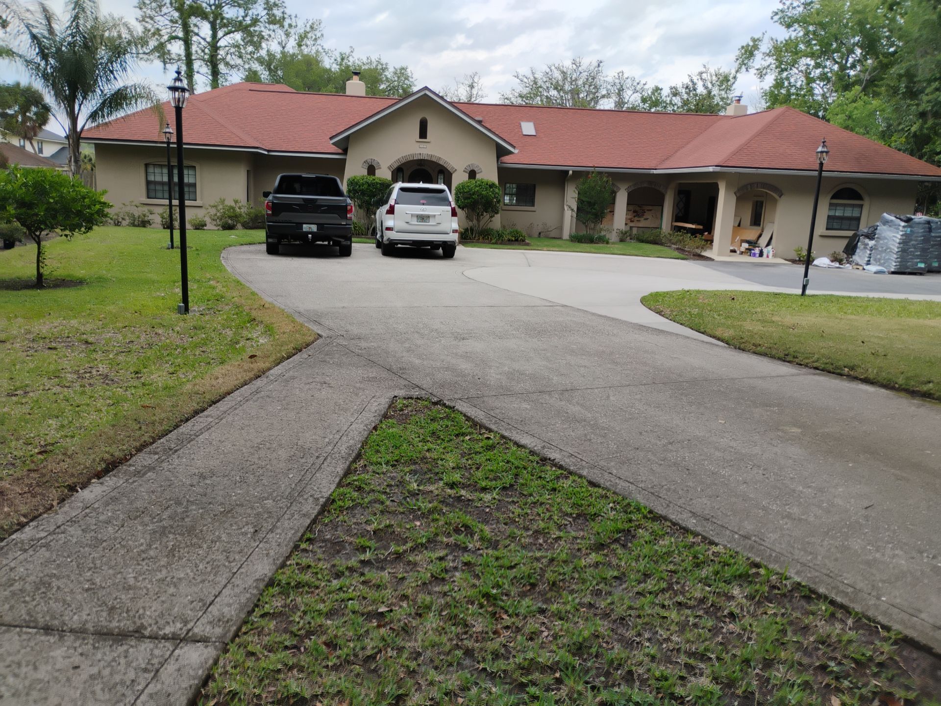 Suburban house with a red roof, driveway, and two parked cars under a cloudy sky