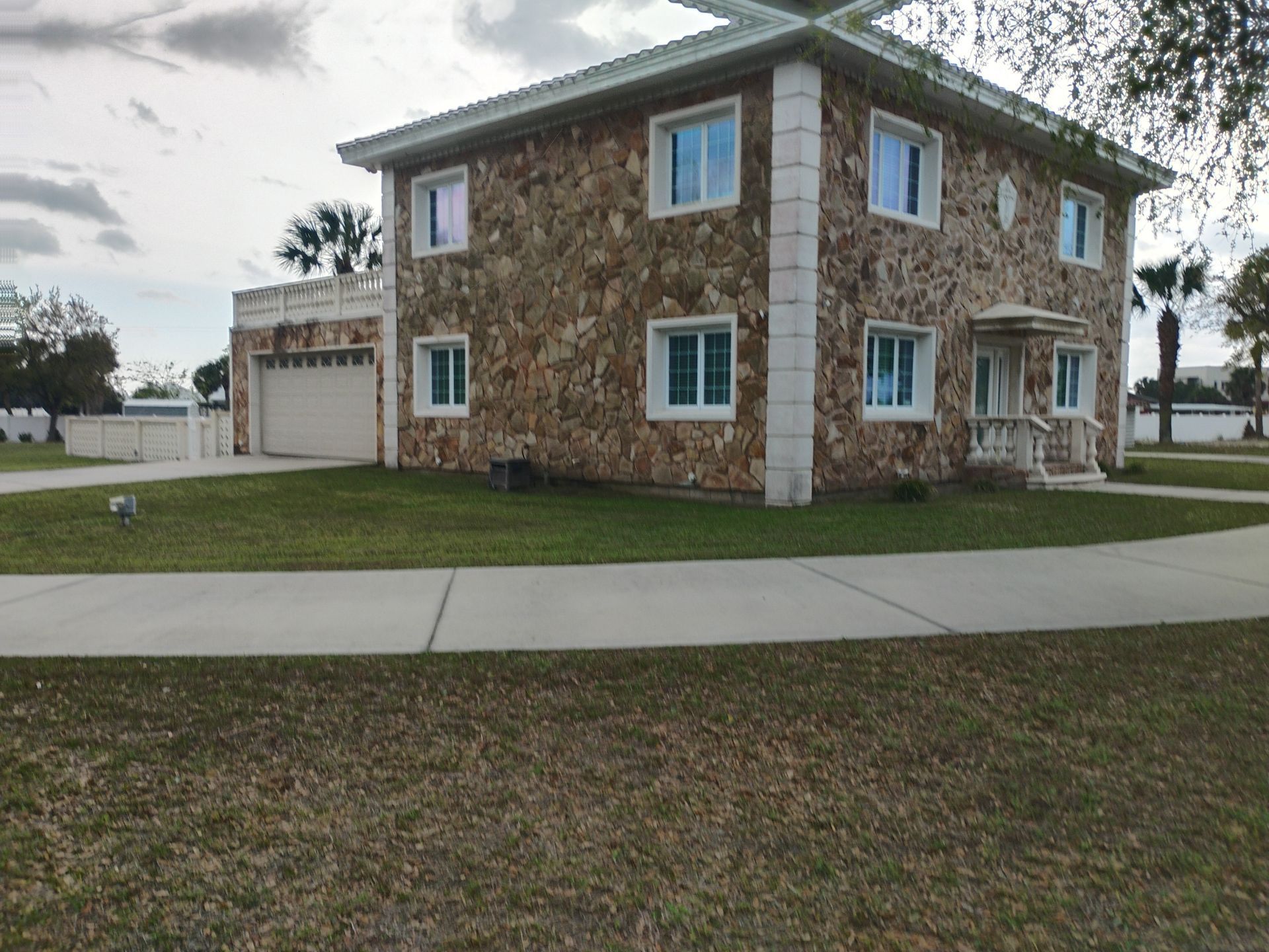 Two-story stone duplex with white trim and garage on a grassy corner lot