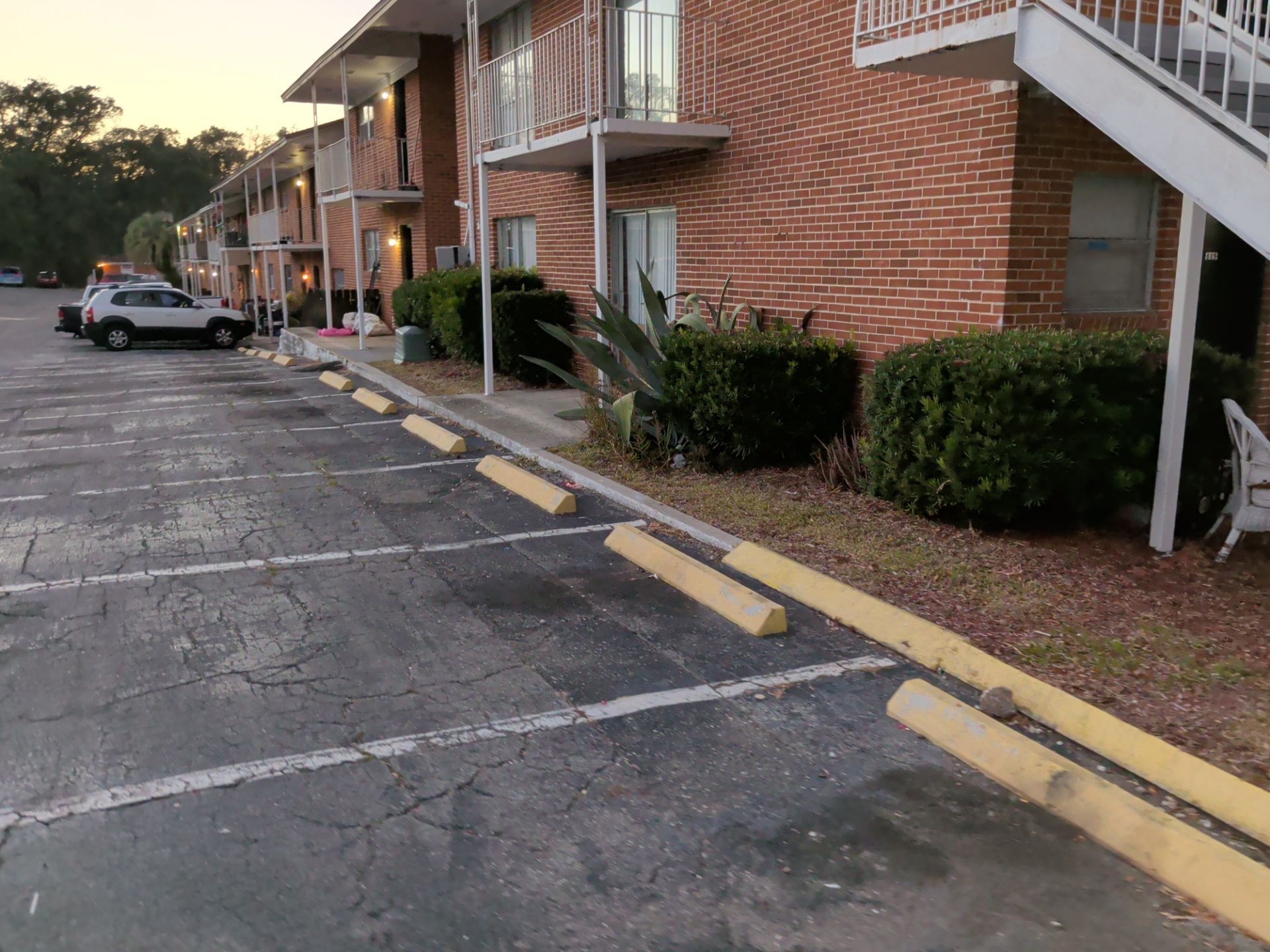 Apartment parking lot beside brick buildings at dusk, with yellow curbs and a parked car in the distance