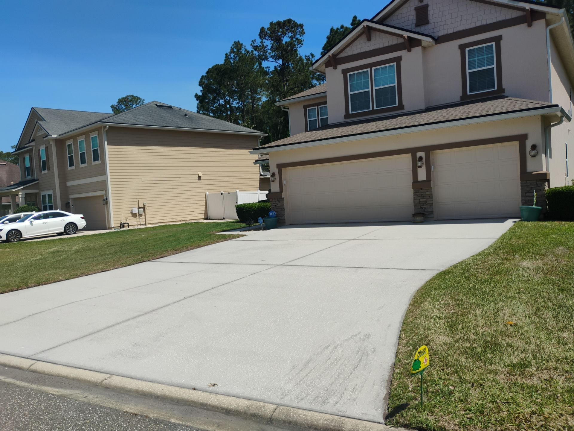 Suburban driveway leading to a two-story beige house with a double garage on a sunny day
