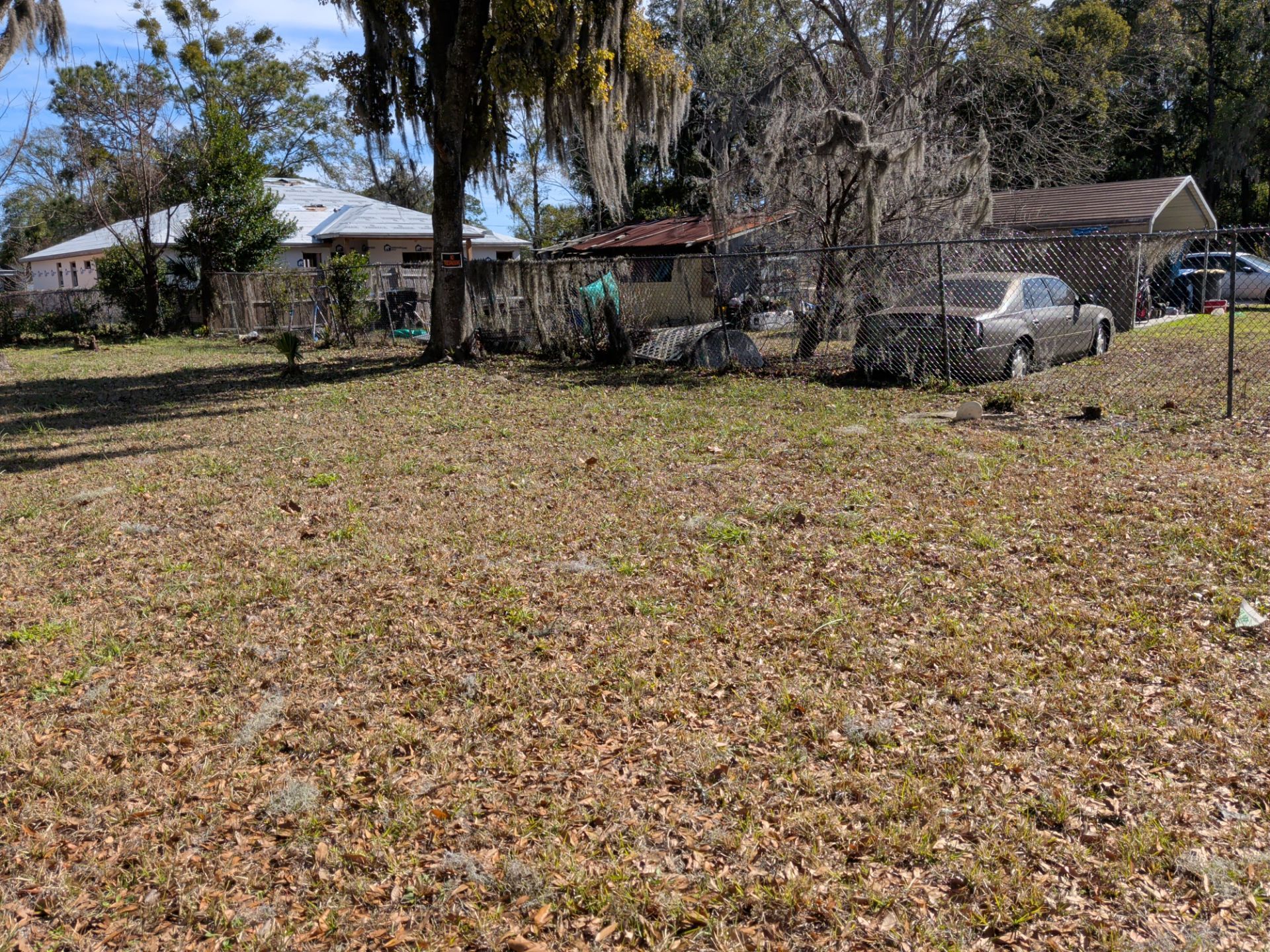 A brown and grassy lot with some trees and a few houses in the background.