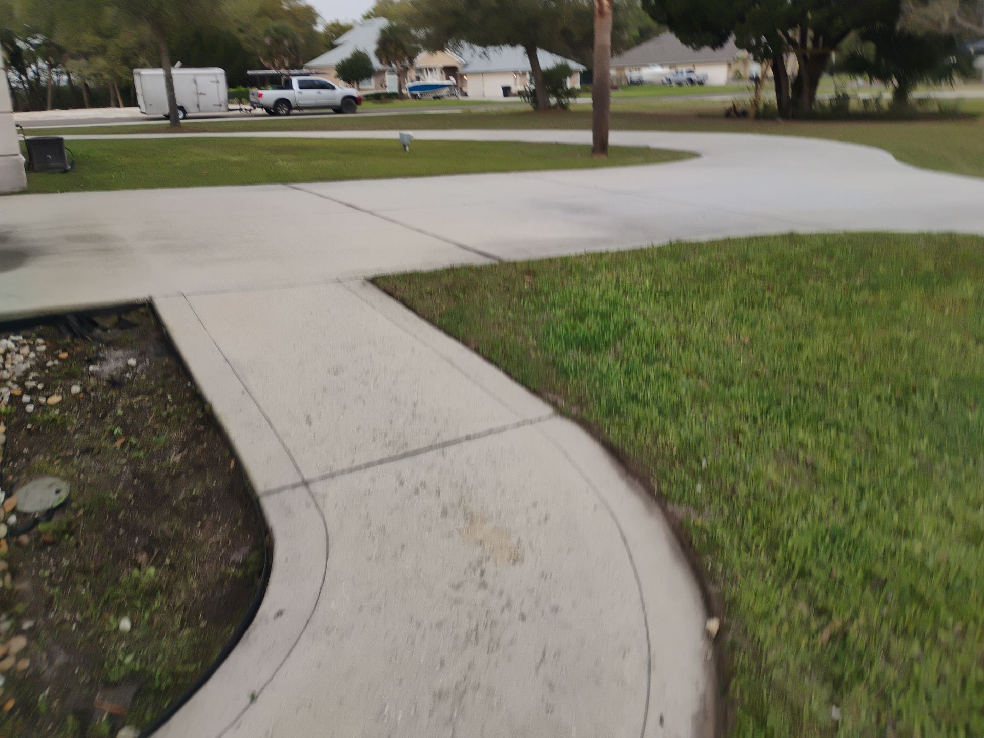 Curved sidewalk through a grassy suburban neighborhood with parked cars in the background
