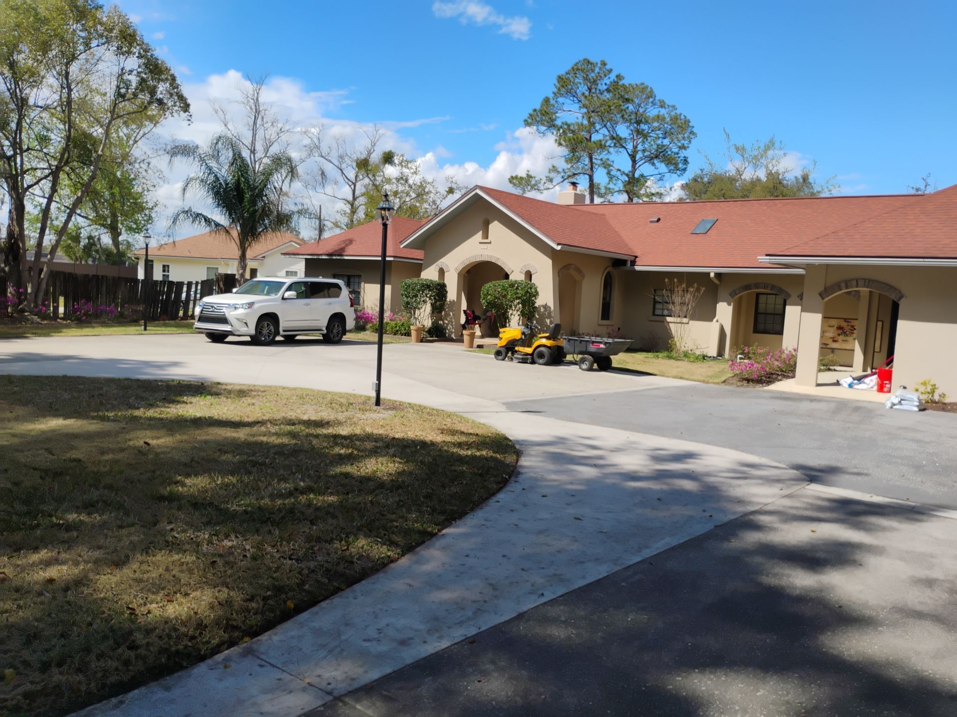 Single-story beige building with red roof, curved driveway, and a white SUV parked outside under a blue sky.