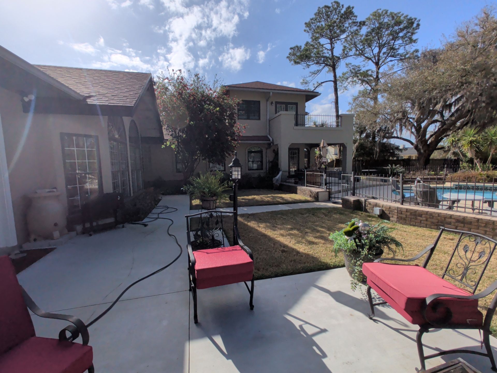 Backyard patio with red cushioned chairs, lawn, pool, and two-story house under a sunny sky