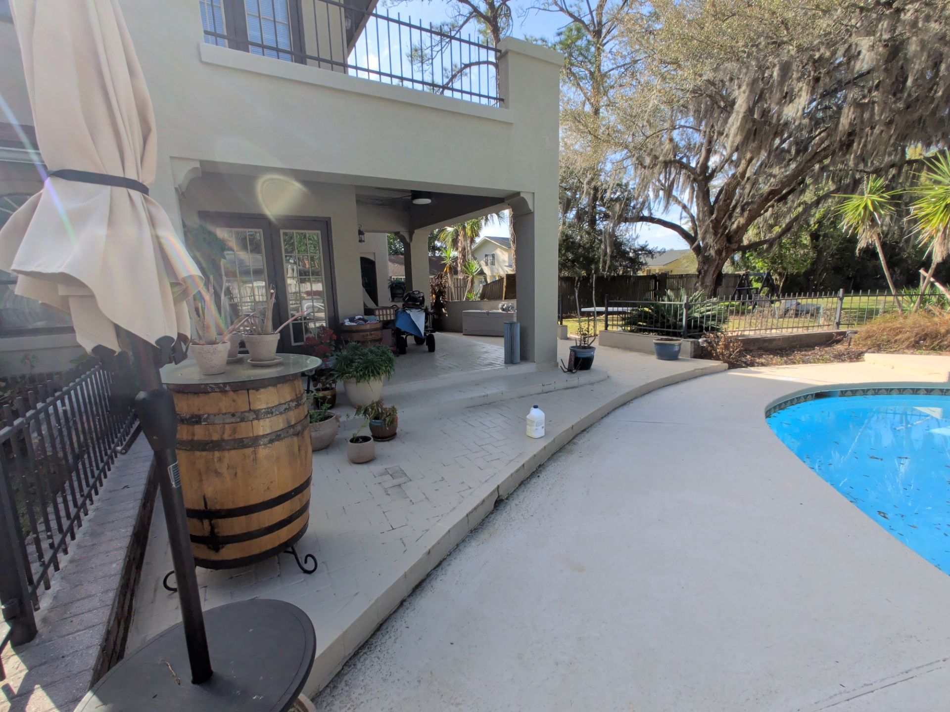 Back patio with covered seating, barrel table, and a swimming pool beside a two-story house