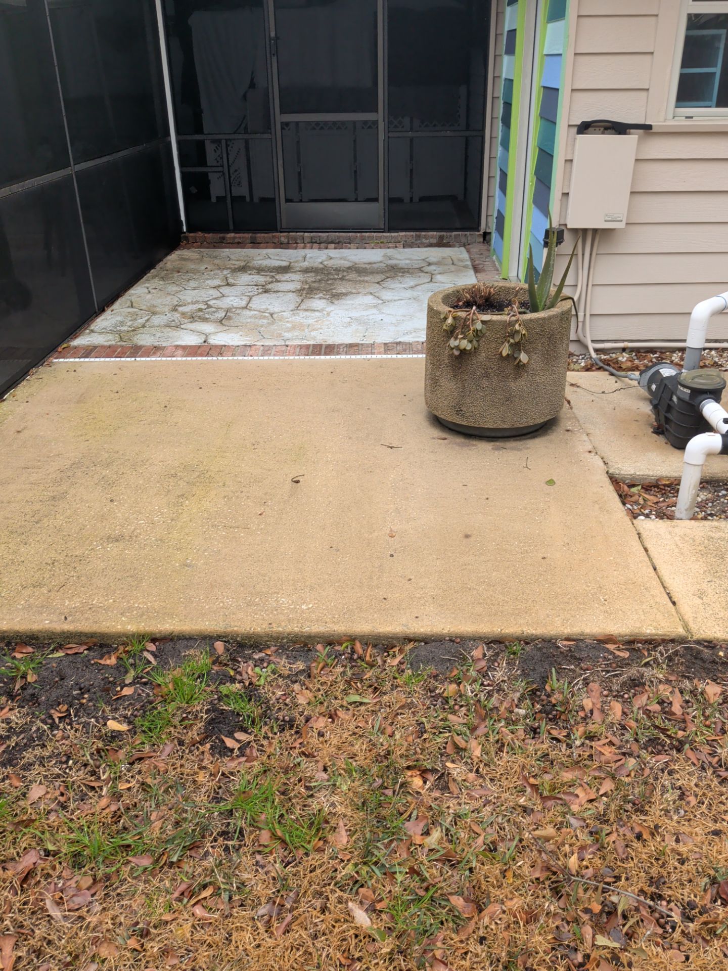Concrete patio with a weathered mat, a potted plant, and an outdoor hose near a house entrance
