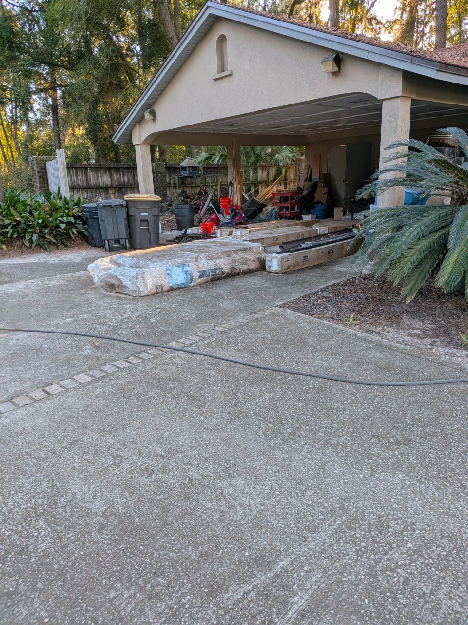 Covered driveway with stone steps, potted plants, and a garage-style carport with items stored inside.