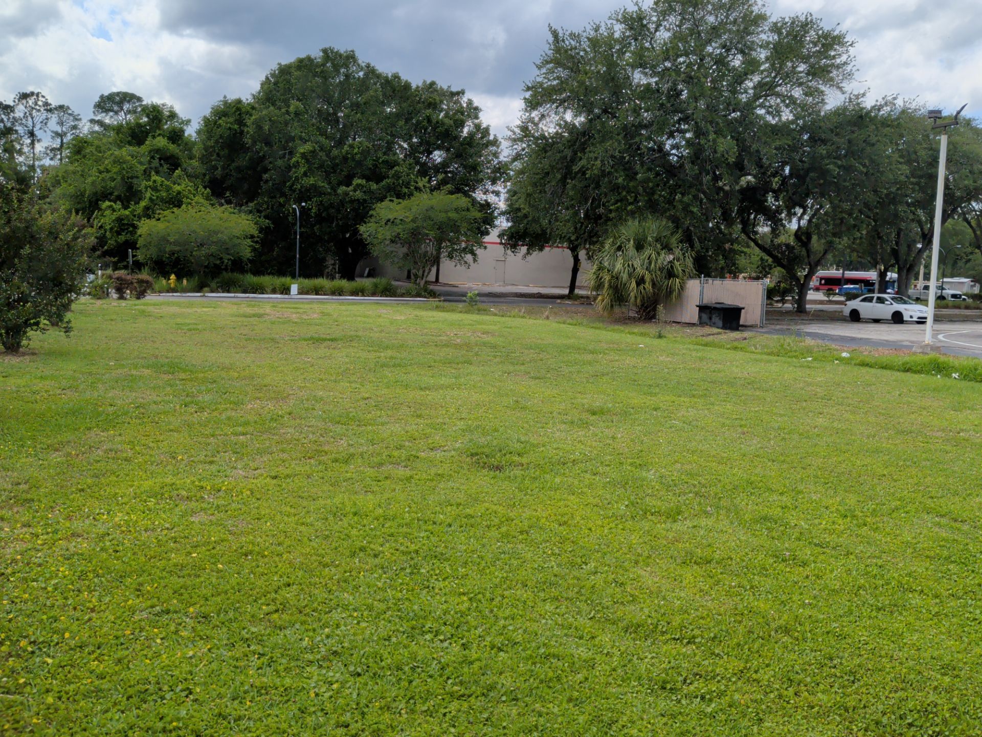 Grassy park with trees, a small building, and a road under a cloudy sky