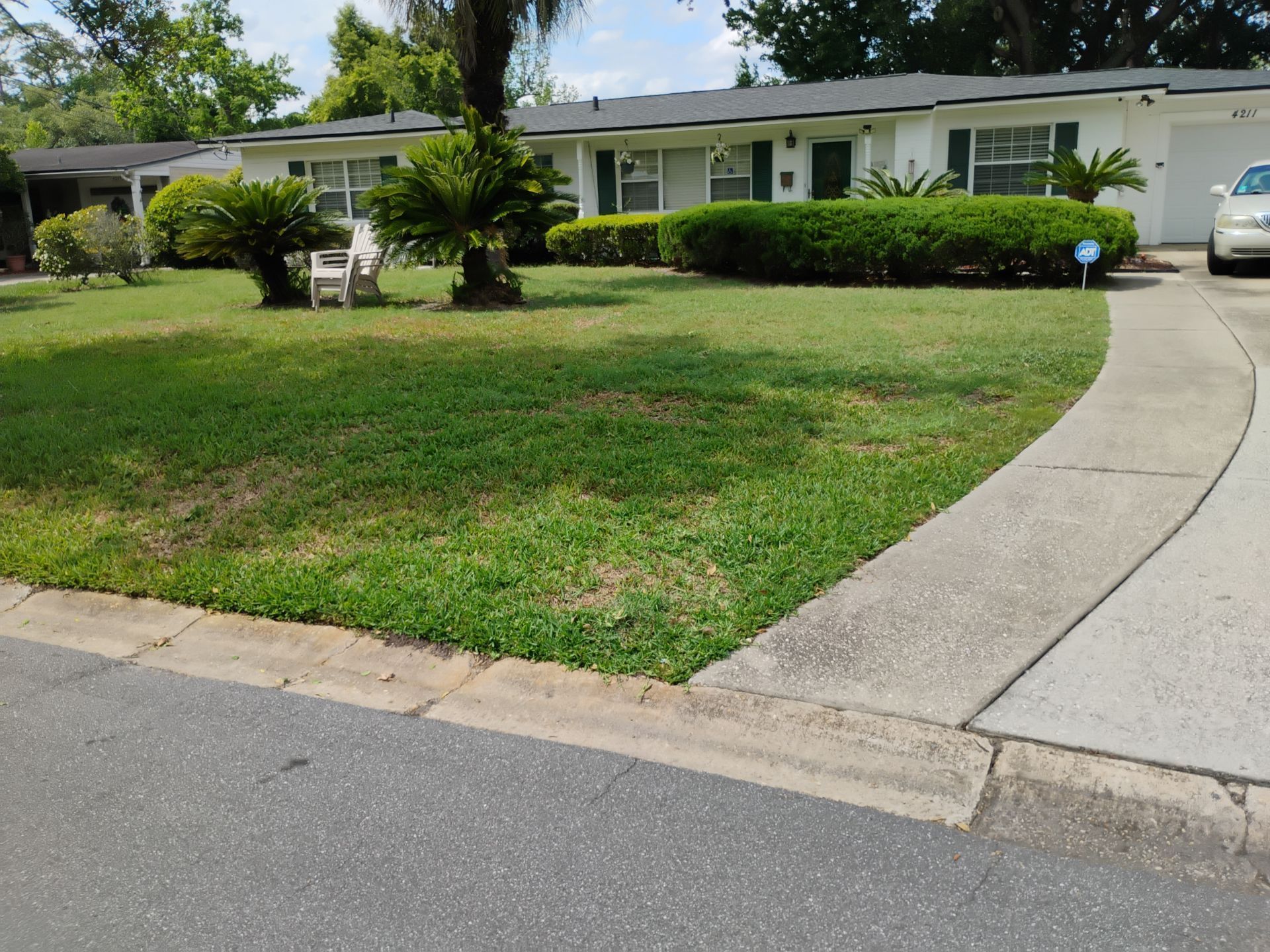 Single-story suburban house with a green lawn, curved driveway, and parked car on a sunny day