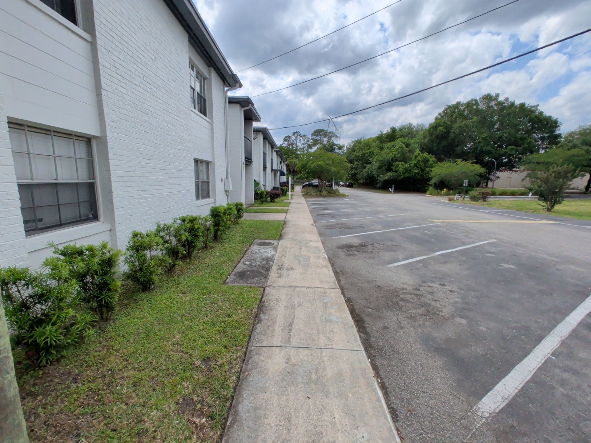 Apartment building beside empty parking lot and sidewalk under cloudy sky