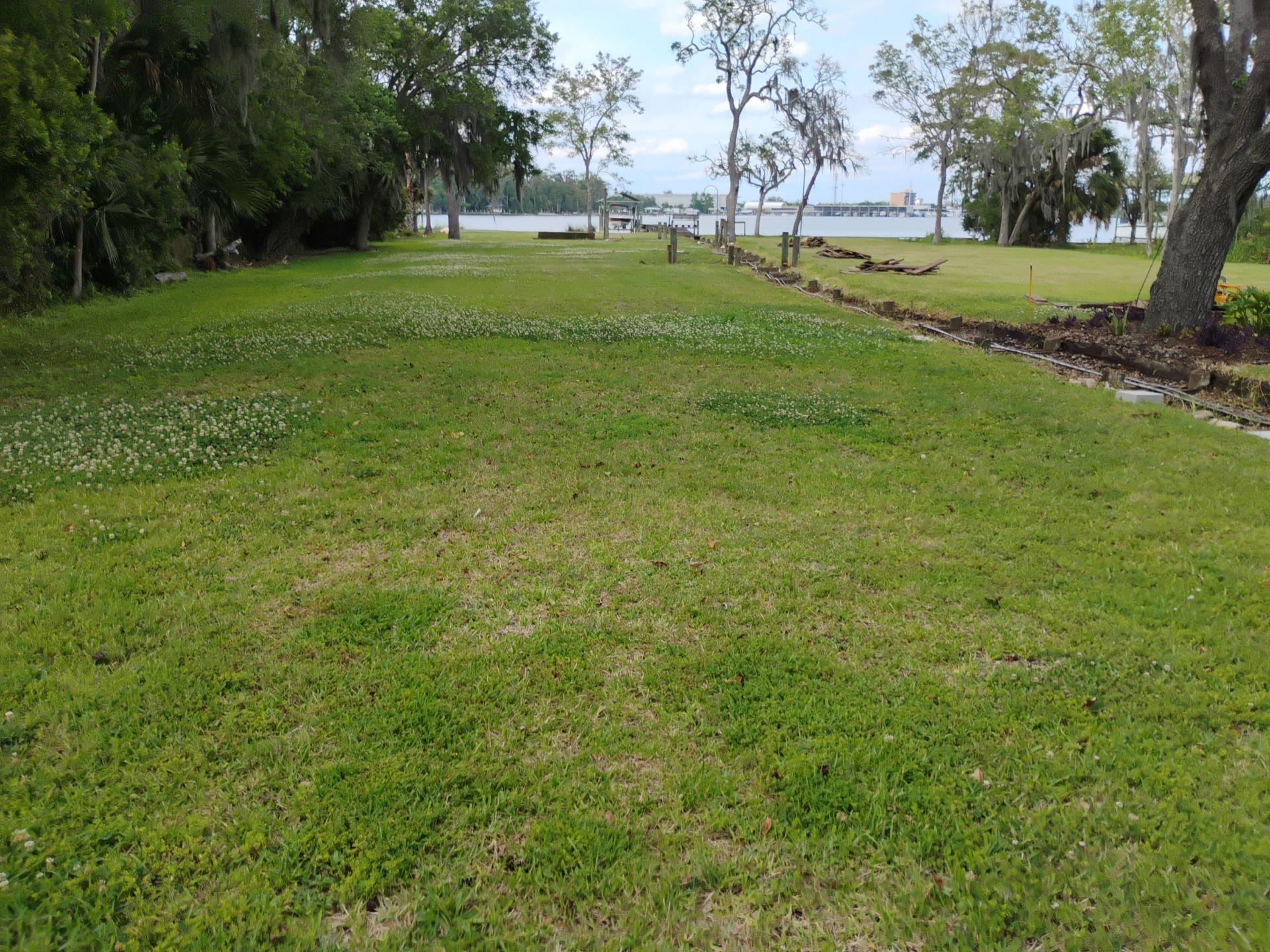 Grassy park path beside trees and a calm waterfront under a cloudy sky