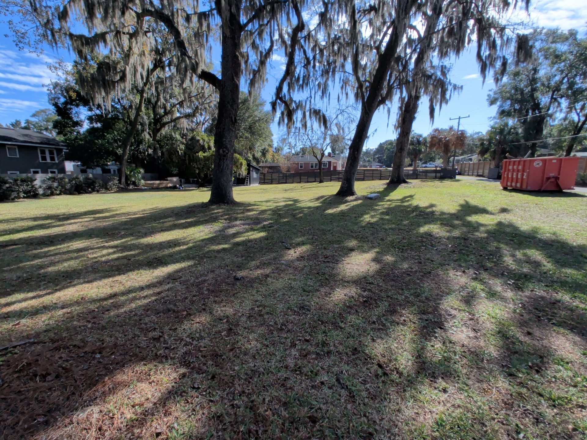 Grassy lot with several trees and a red dumpster under a bright blue sky.