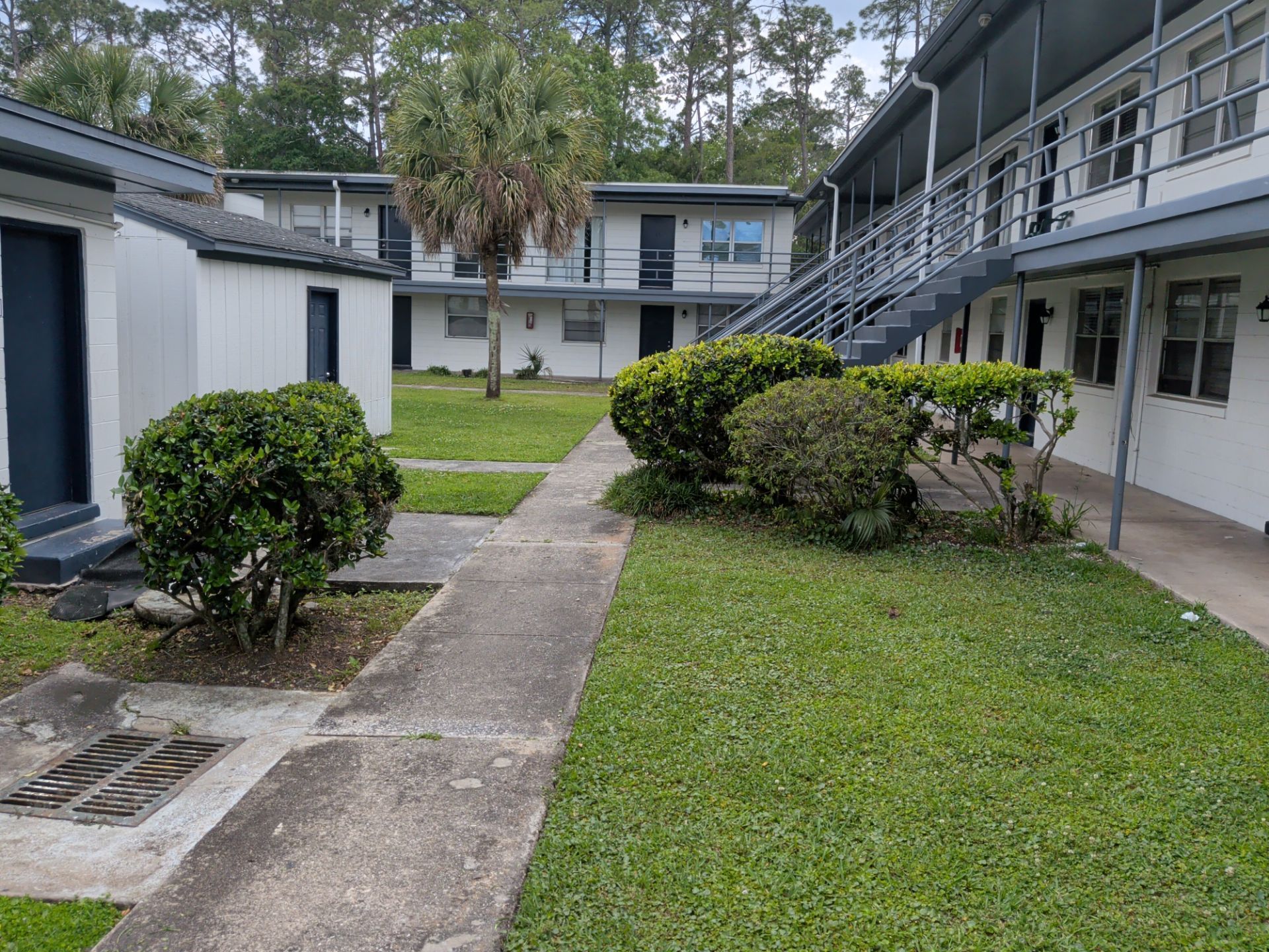 Courtyard between apartment buildings with grass, shrubs, and concrete walkways under a cloudy sky