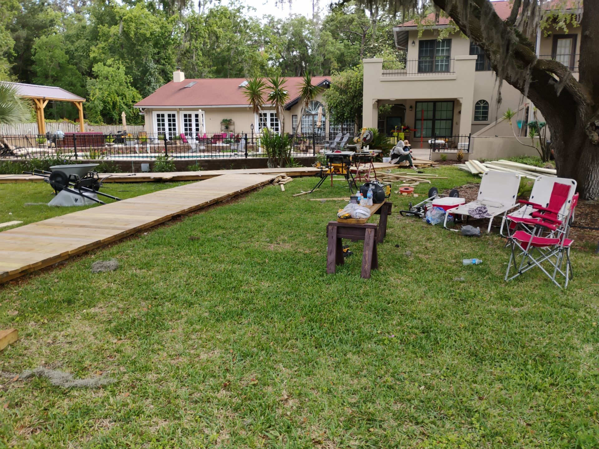 Backyard with lawn chairs, table, walkway, and houses under trees