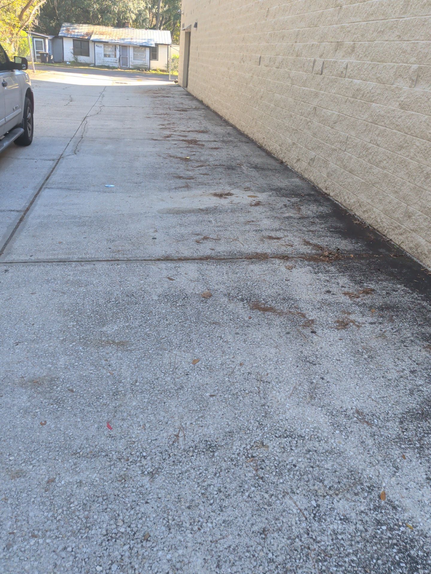 Concrete alleyway next to a beige building wall. A parked vehicle is on the left side, small structures in the distance.