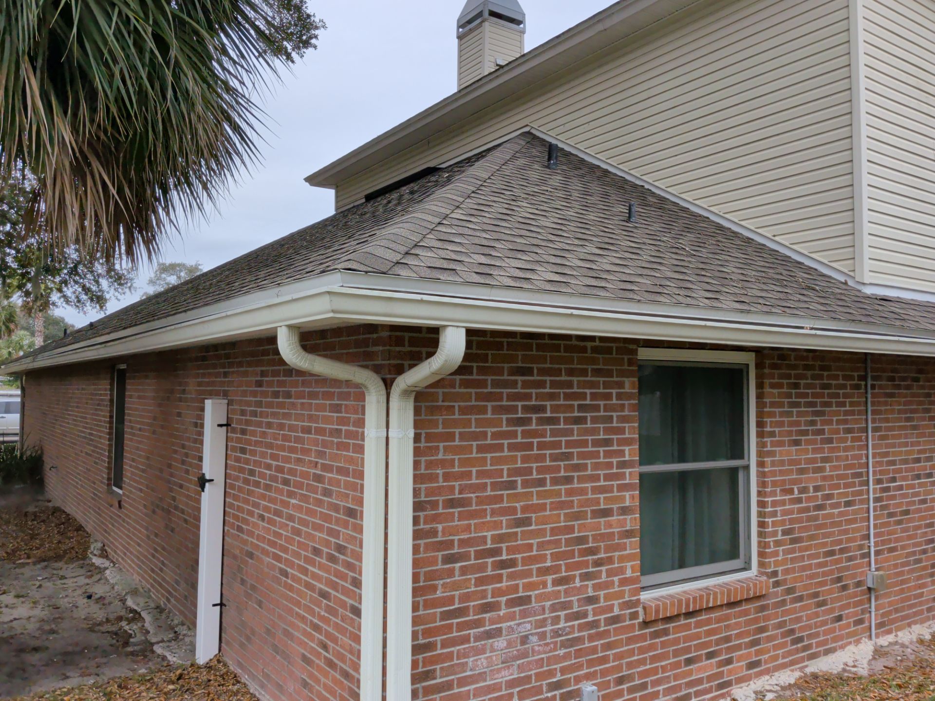 Brick house exterior with brown siding, white gutter, and a window under a sloped roof