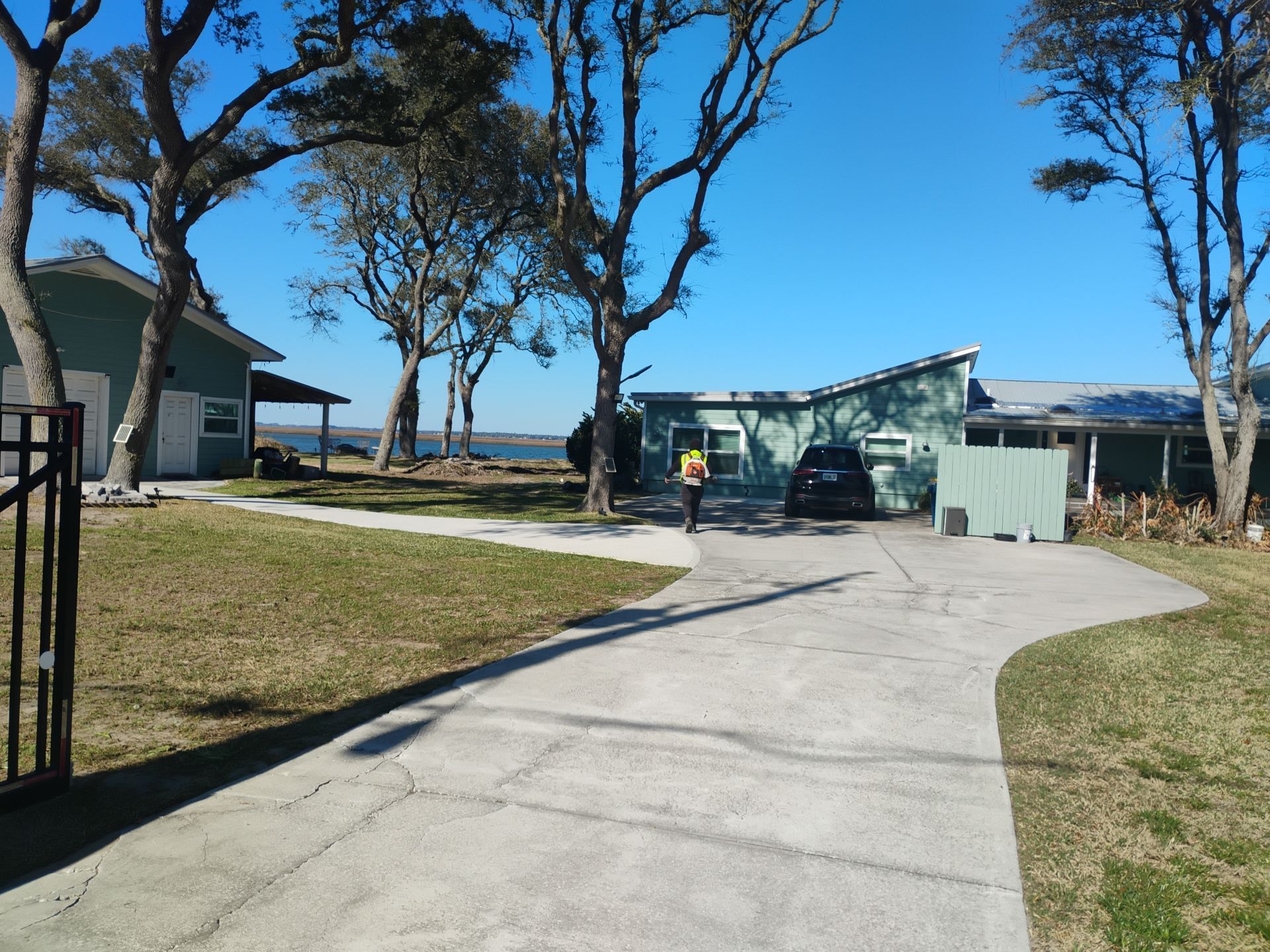Coastal driveway leading to a small house, trees, and a parked car under a clear blue sky.