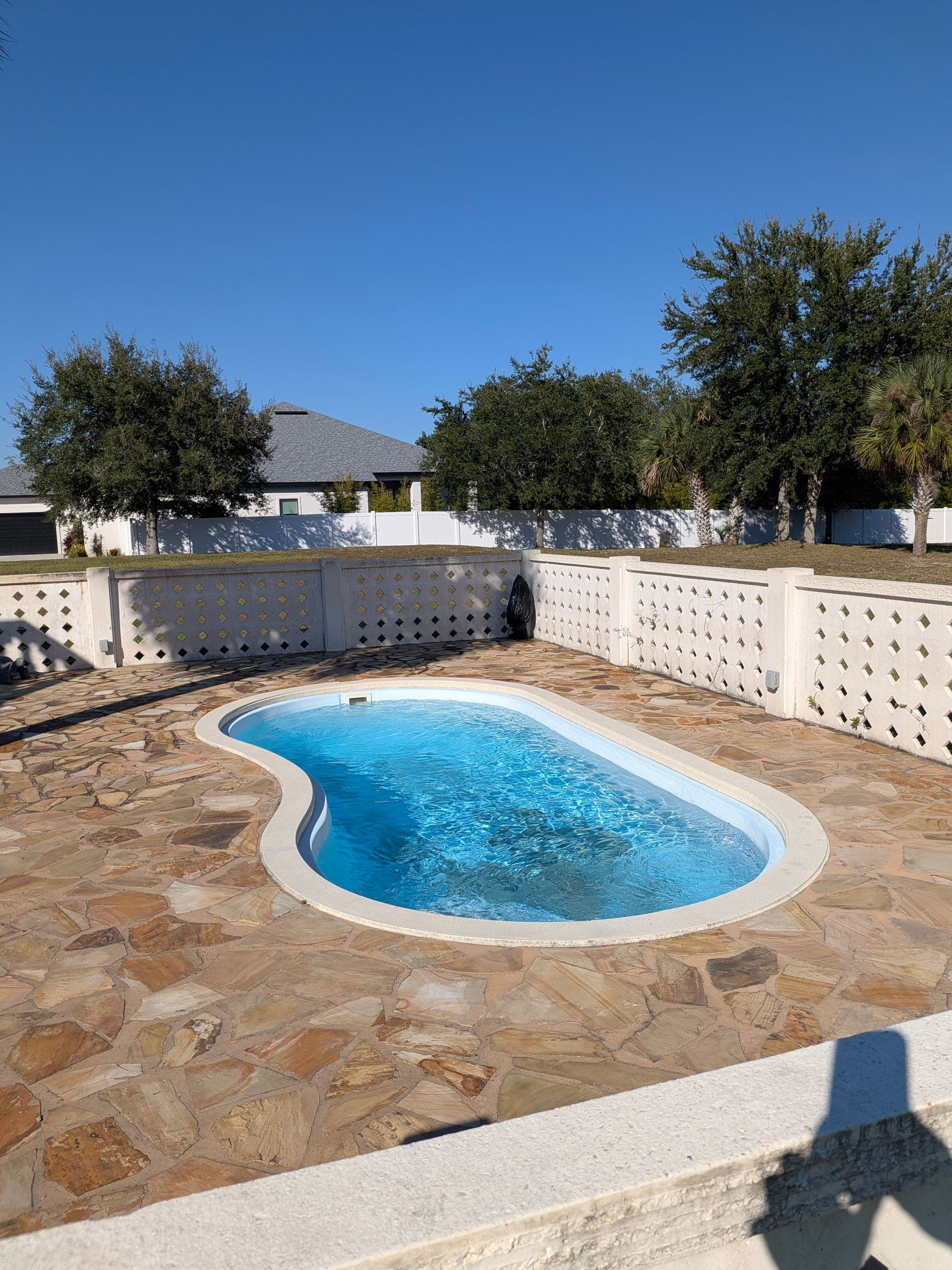 Small blue pool in a stone courtyard with white walls and trees under a clear sky