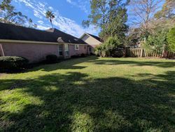 Lawn in a backyard with a house, trees, and fence on a partly cloudy day.