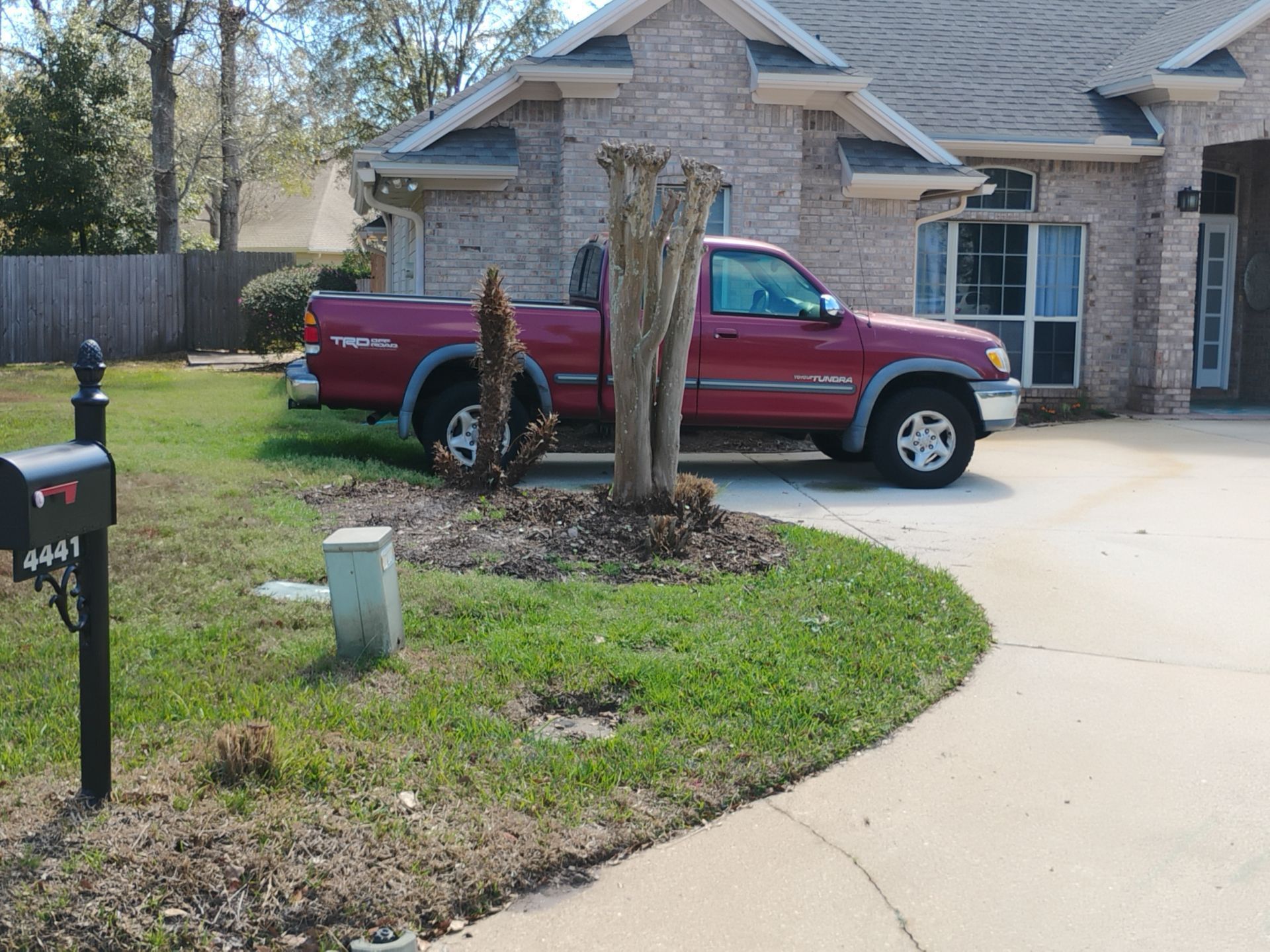Red pickup truck parked in a driveway beside a brick house and front yard tree stump