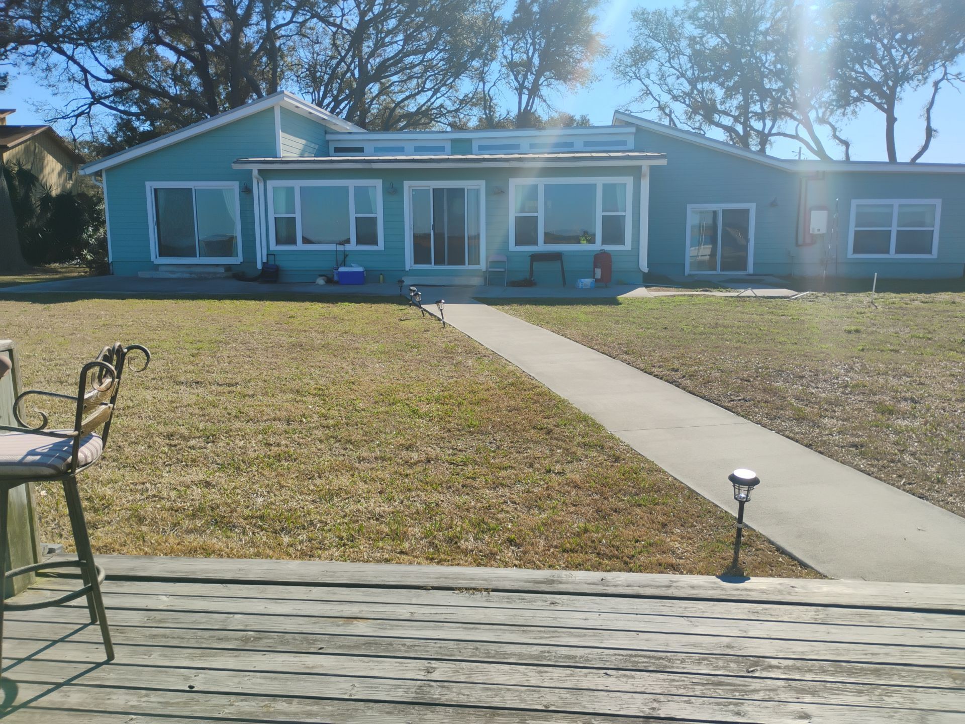 Blue single-story house with a front lawn, concrete walkway, and porch seating on a sunny day