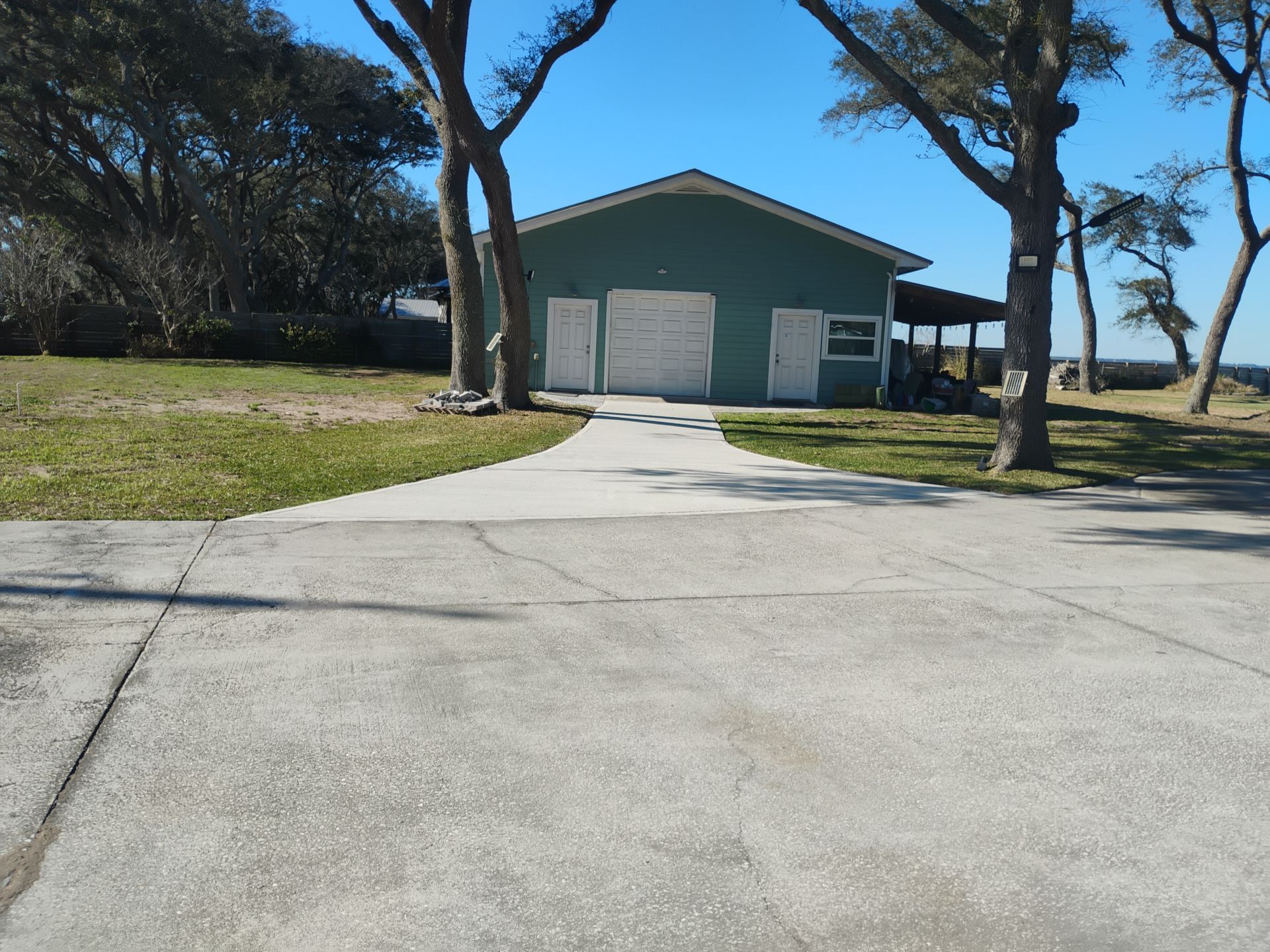 Blue house with white garage doors at end of a driveway, framed by trees and lawn.