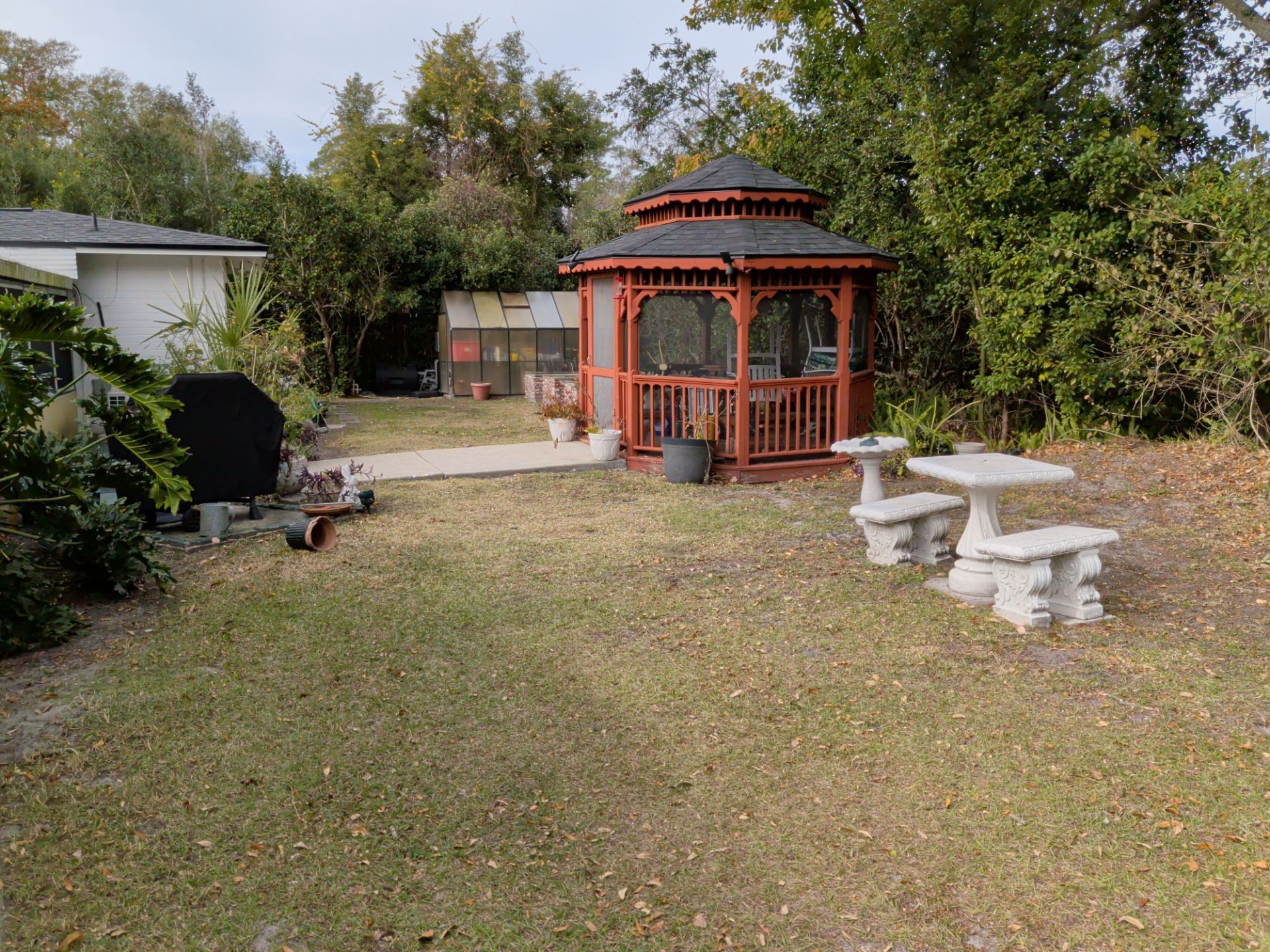 Backyard with red gazebo, stone benches, and trees under a clear sky