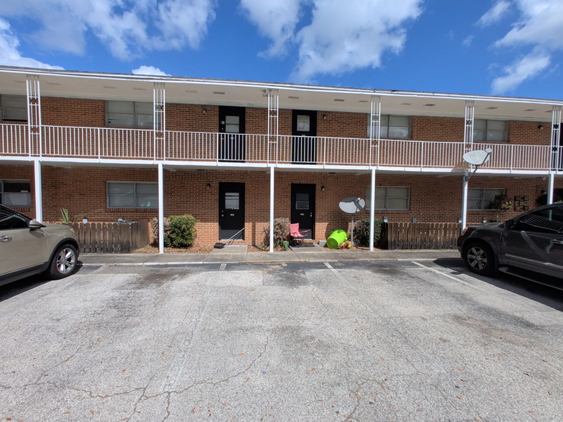 Two-story brick apartment building with parked cars and a few people sitting on the front walkway