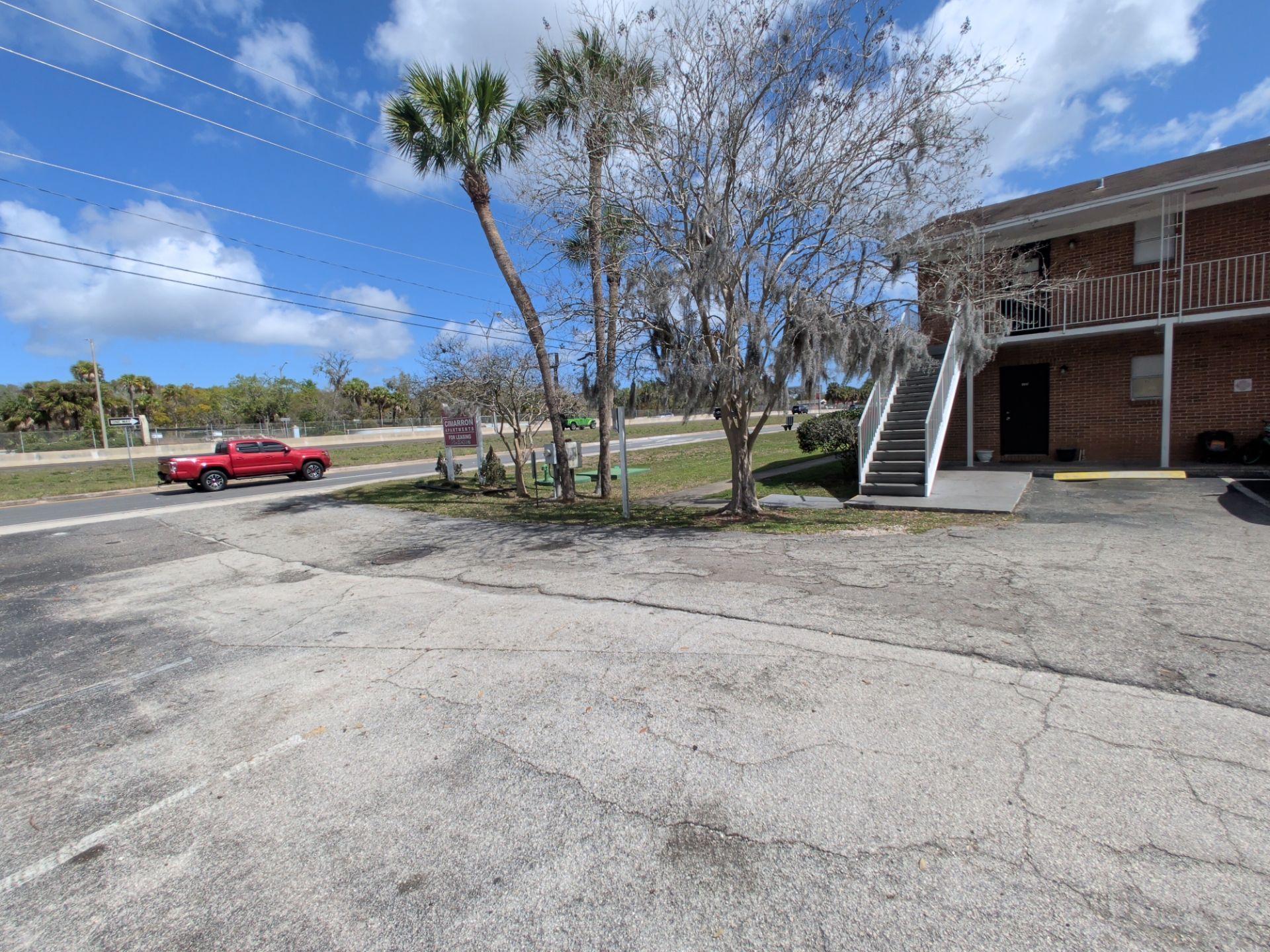 Apartment parking lot with a red car, trees, and a brick building with exterior stairs