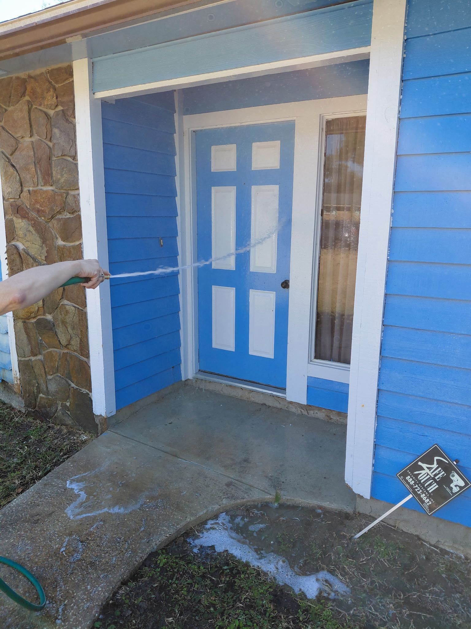 Person spraying a blue and white front door with a hose, cleaning the entrance.